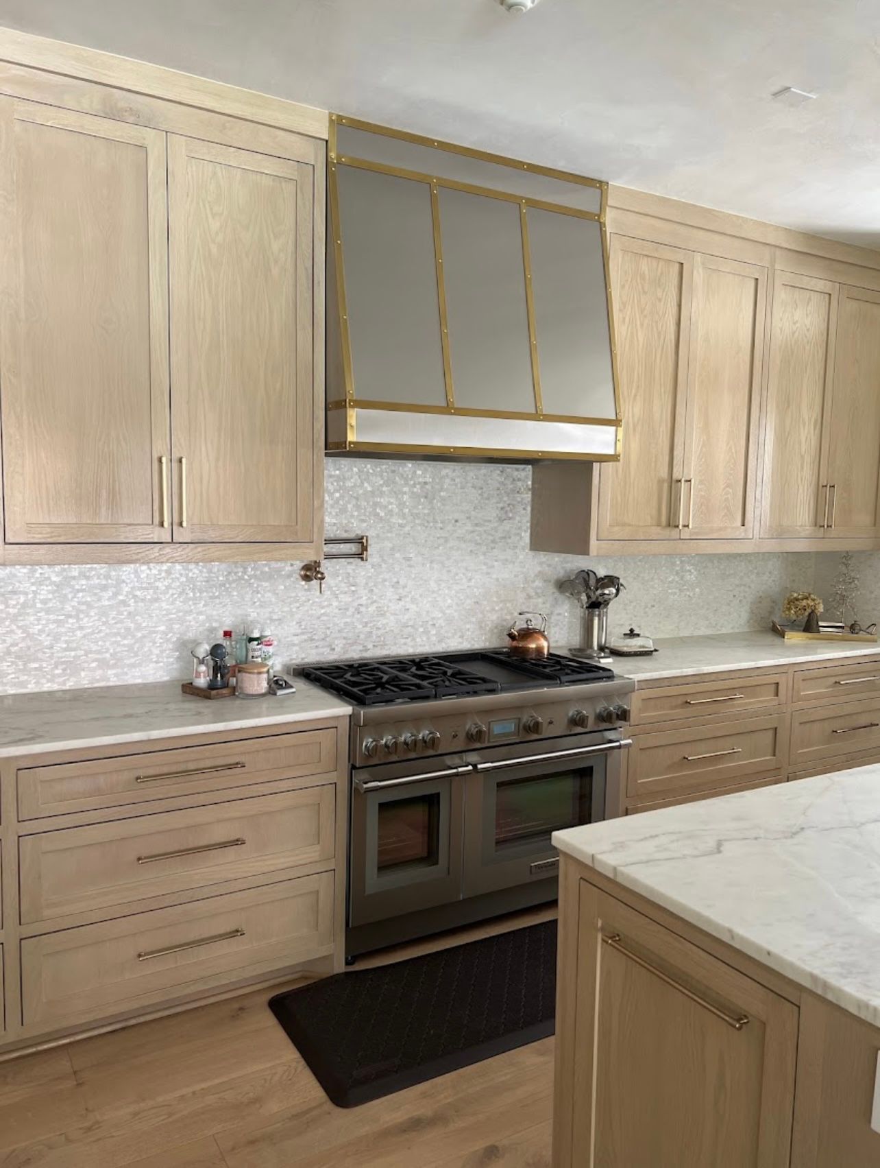 Modern kitchen with beige cabinets, marble countertops, and a stainless steel stove under a gold-trimmed hood.