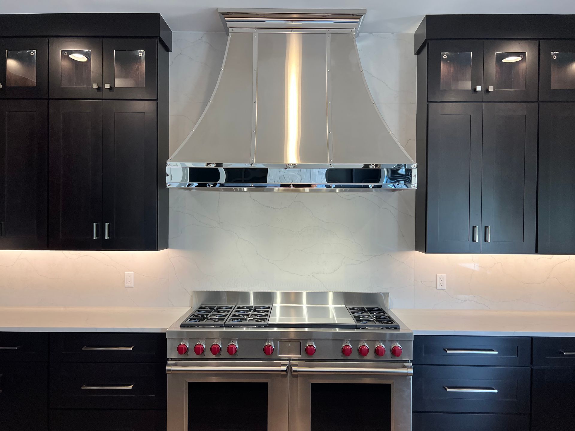 Modern kitchen with stainless steel range and hood, dark wood cabinets, and white backsplash