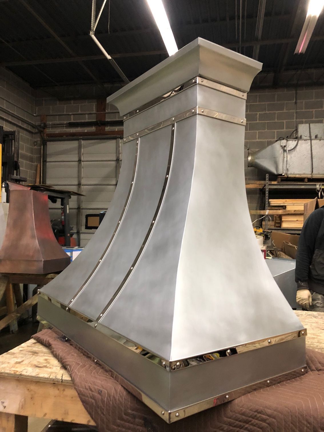 Metal industrial hood or chimney assembly in a workshop, silver with riveted seams on a wooden workbench