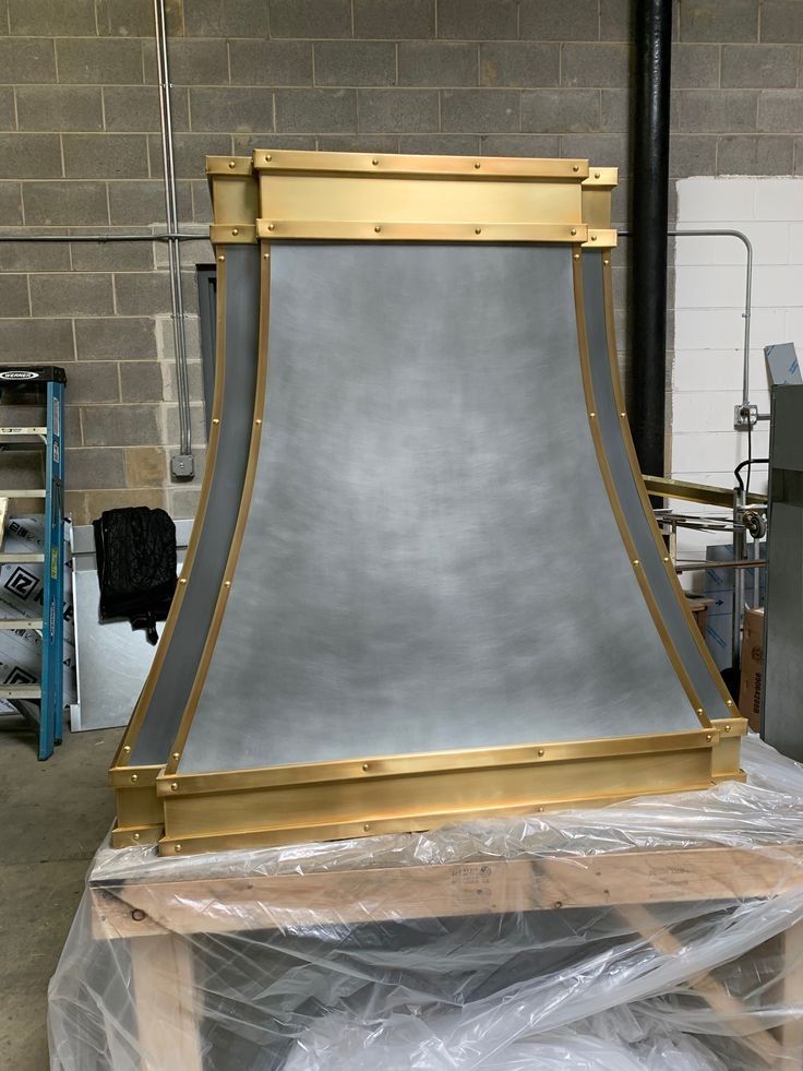 Large metal curved panel with gold trim in a workshop, wrapped in plastic on a pallet.