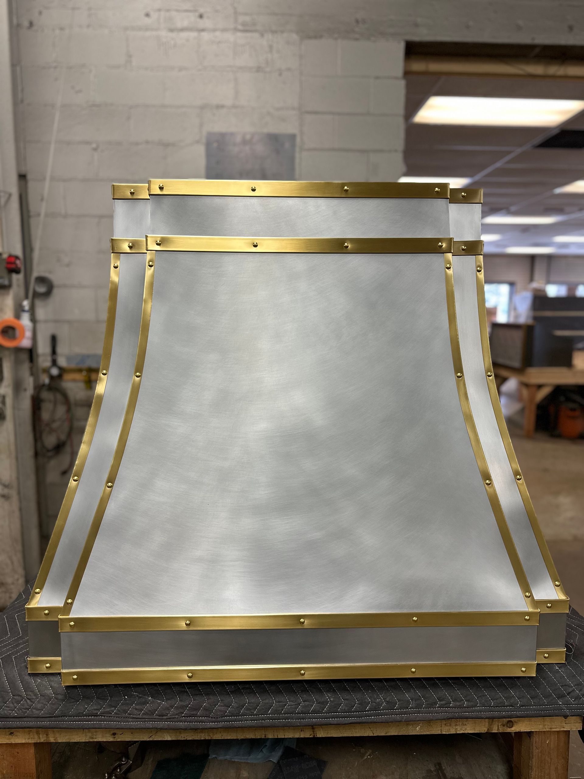 Brass-edged metal lamp shade on a workshop table, with a tapered silver surface.