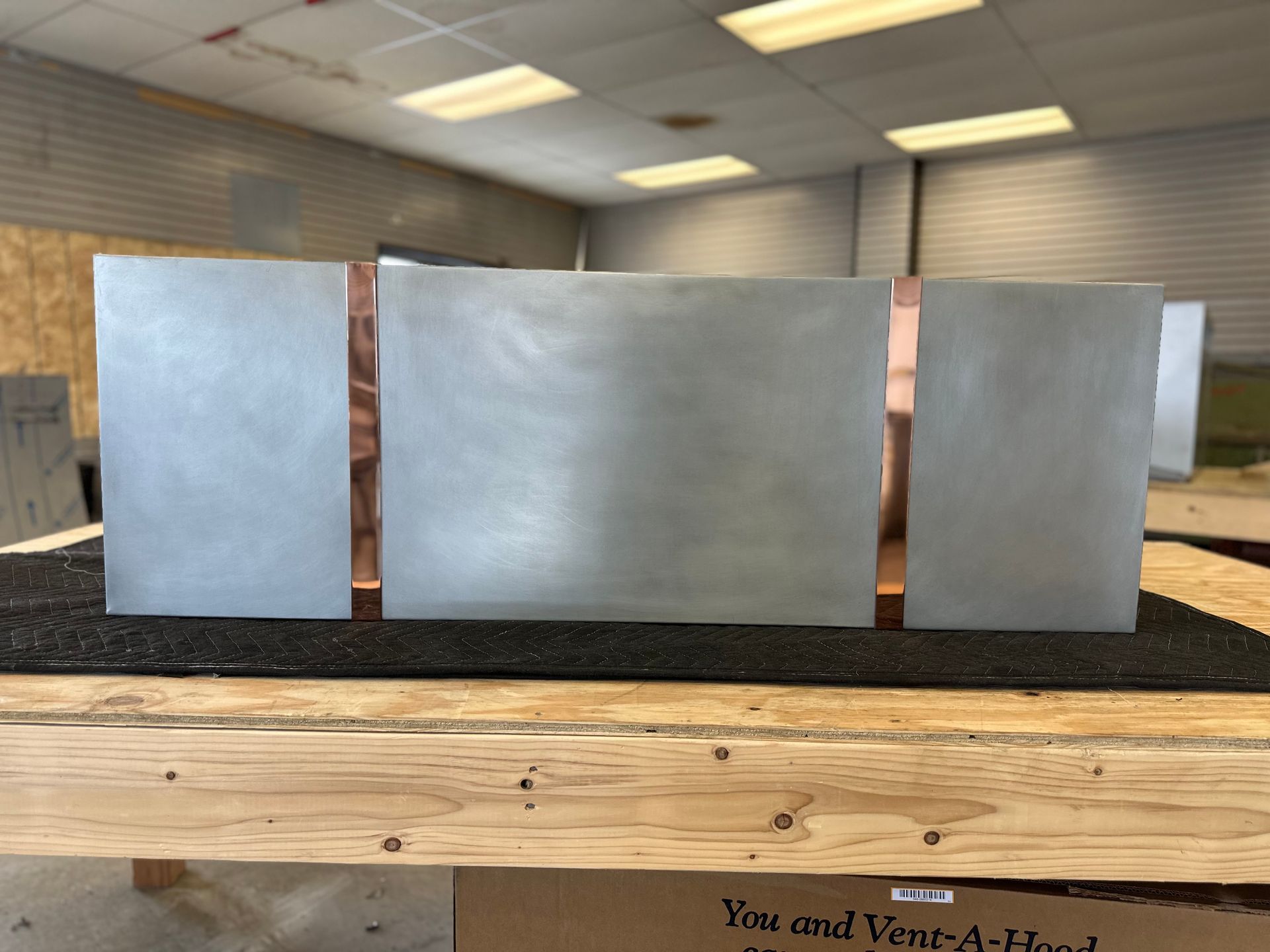 Three blank silver metal panels displayed on a wooden table in a workshop.