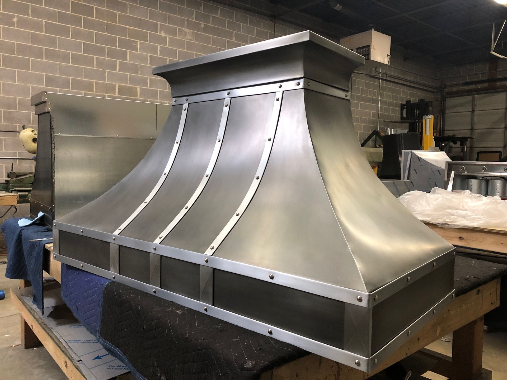 Large stainless steel industrial hood on a pallet in a workshop.
