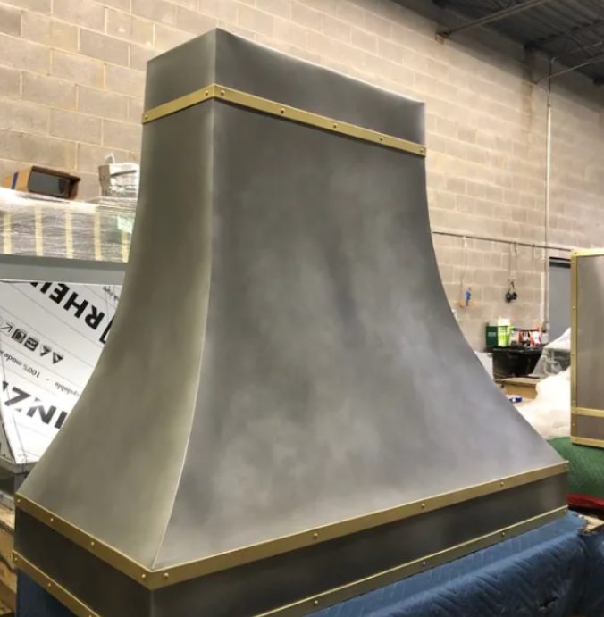 Gray metal chimney hood in a workshop, with gold trim on a blue-covered surface.