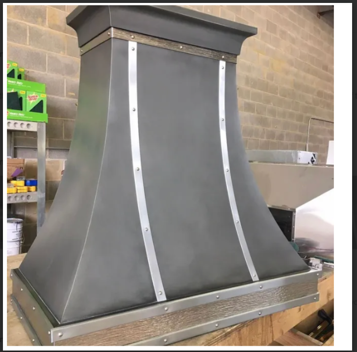Stainless steel range hood with dark gray panels in a workshop or kitchen setting