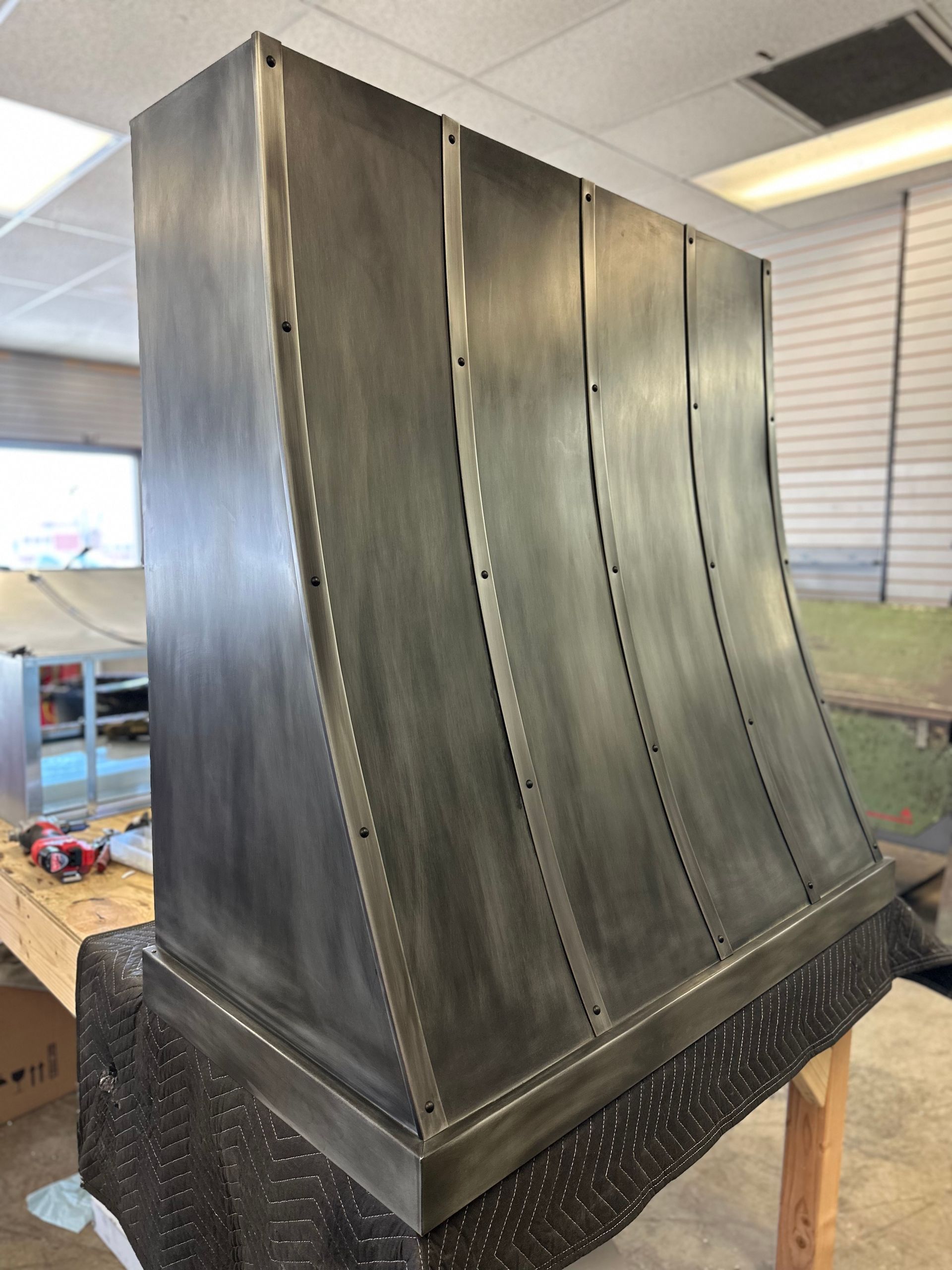 Large brushed-metal industrial hood or duct with riveted panels on a workbench in a workshop