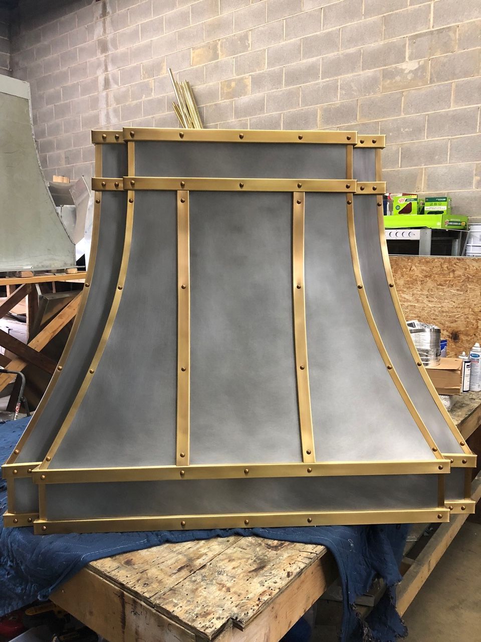 Metal chimney hood under construction with gray panels and wood supports in a workshop