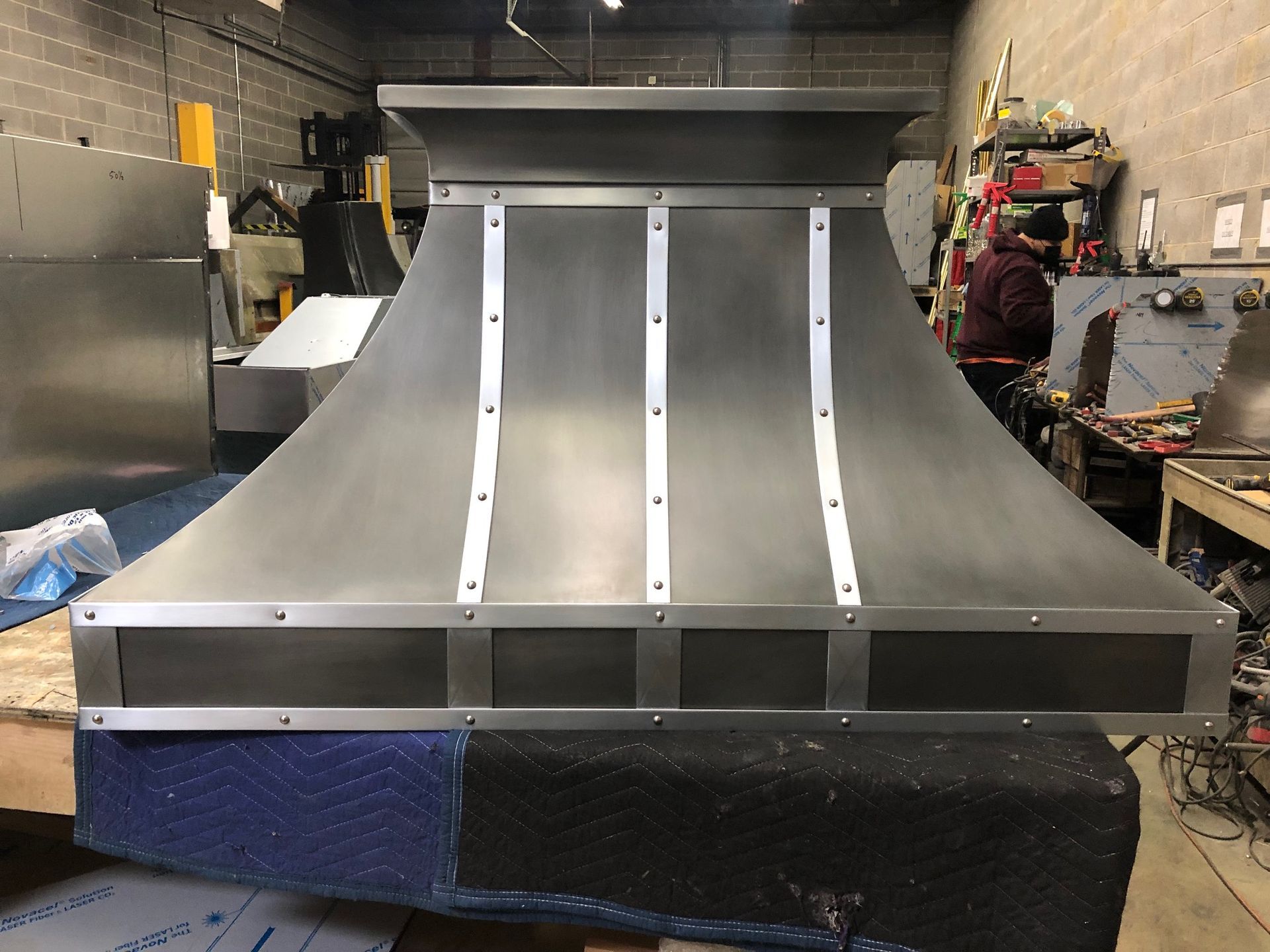 Stainless steel custom curved ramp or chute in a workshop, with white support strips and a blue base.