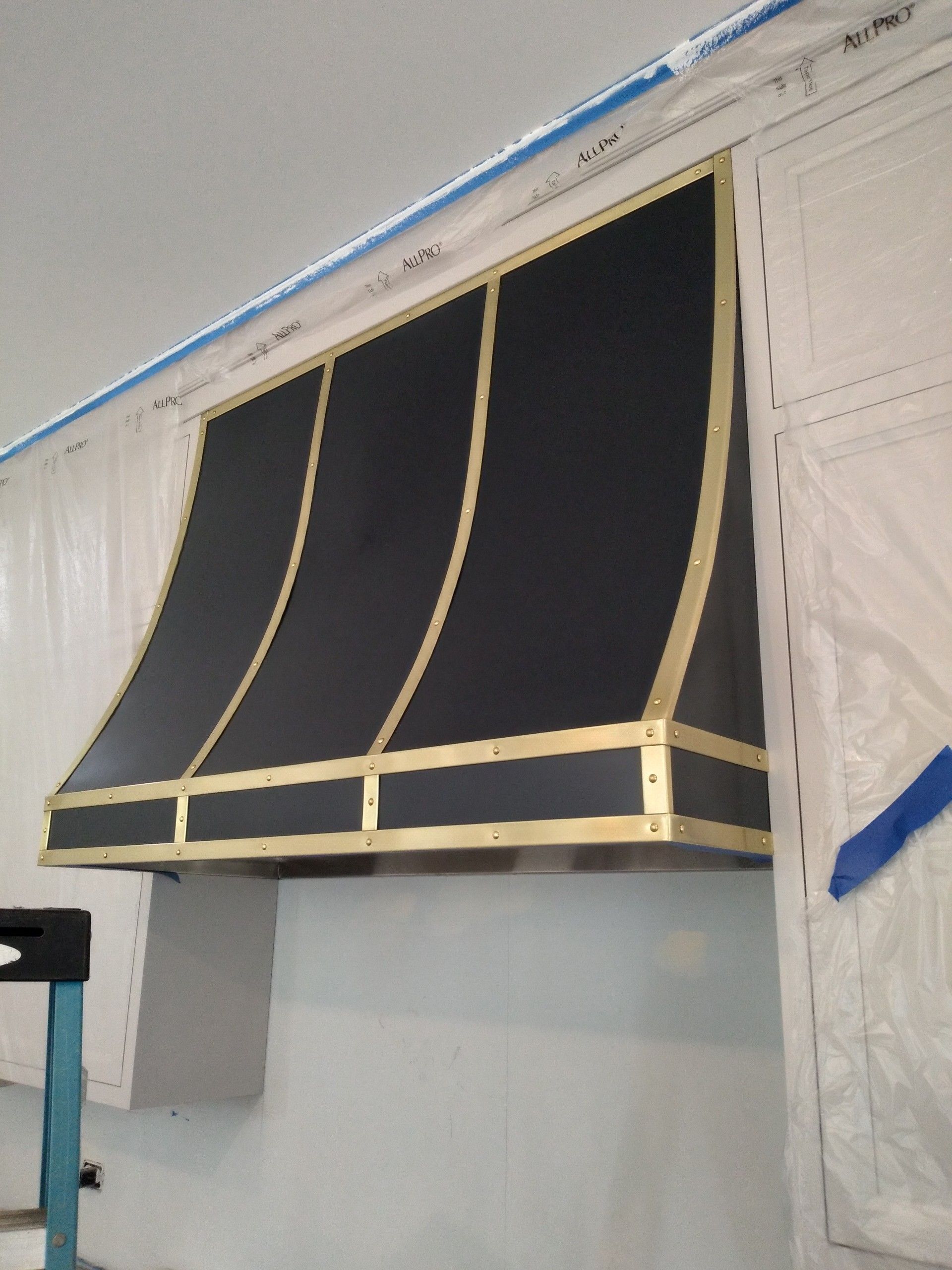 Black awning with tan trim mounted over a window on a white building wall
