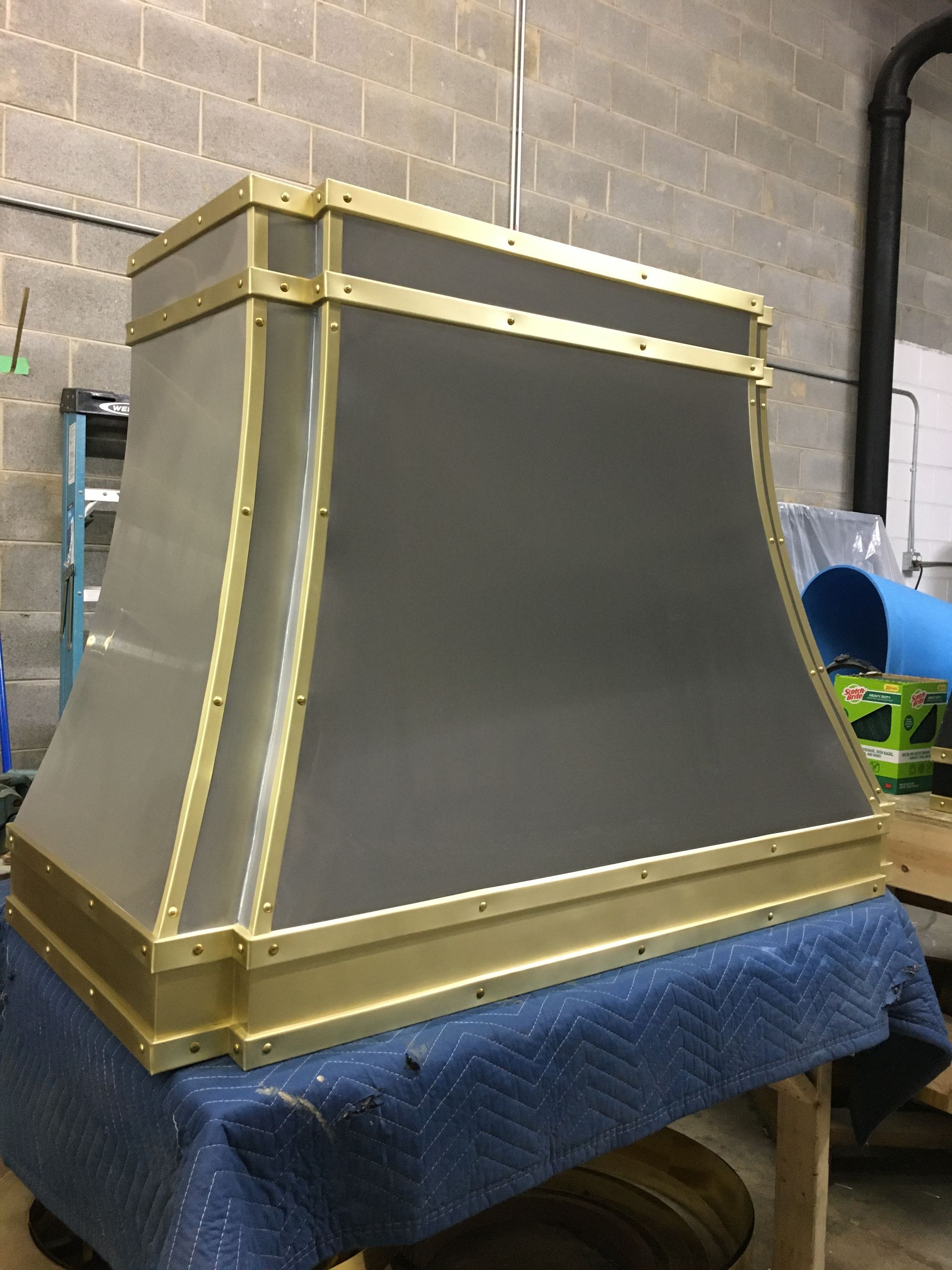 Gold-trimmed gray fireplace mantel on a blue padded surface in a workshop-like room