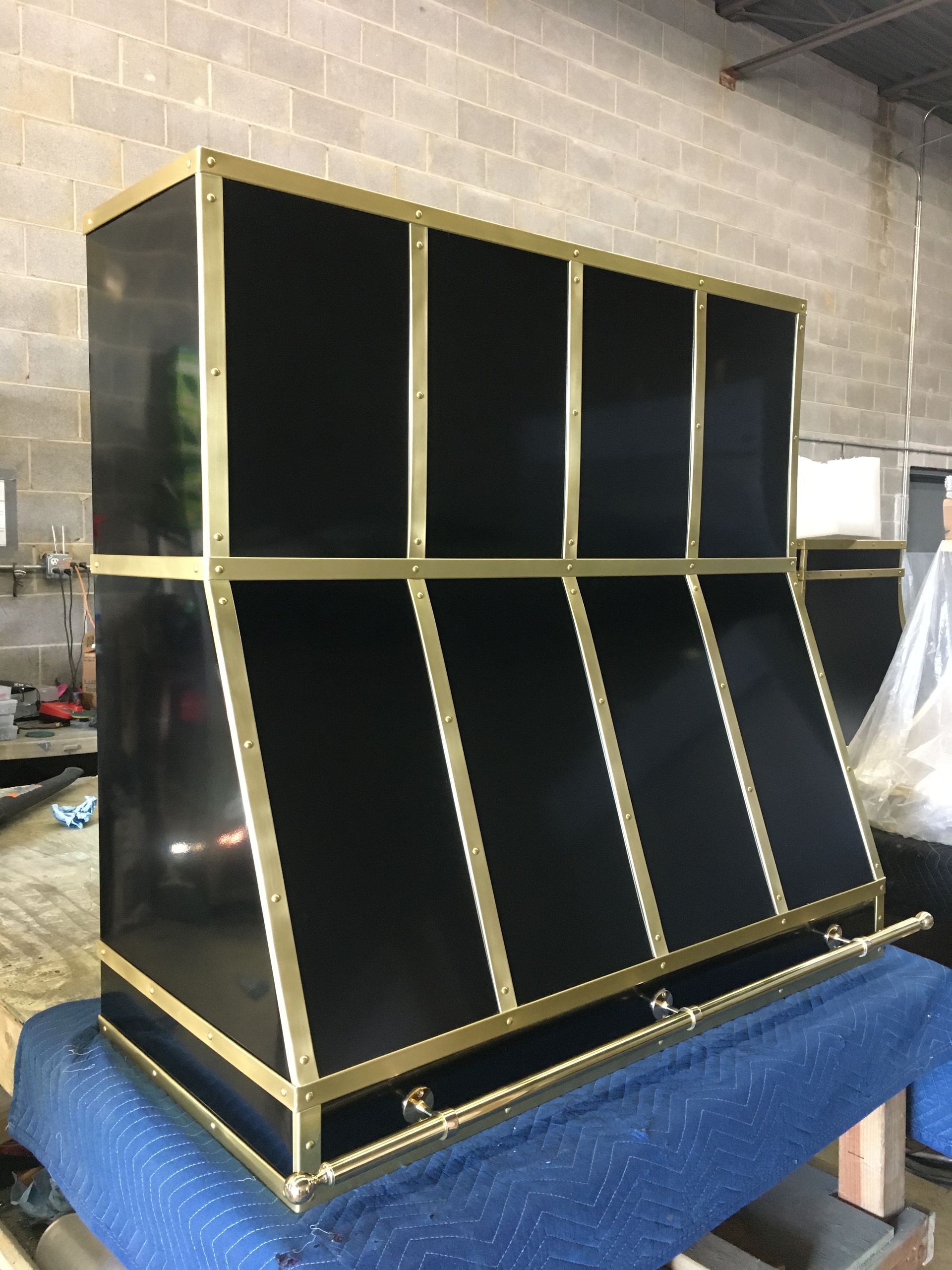 Black and gold geometric cabinet with angled lower panels, sitting on a blue workbench in a workshop