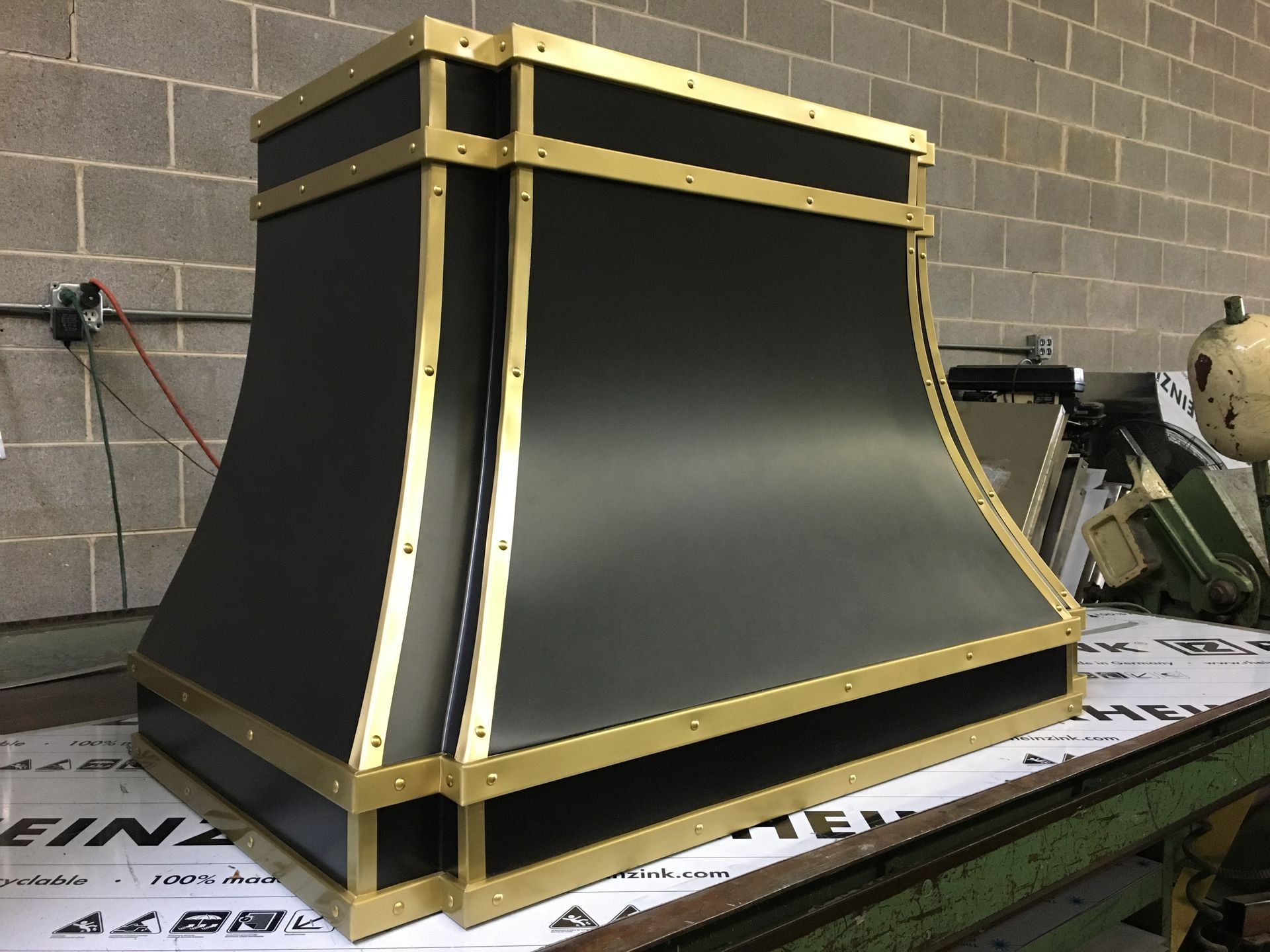 Black-and-gold metal machine enclosure or hopper in a workshop, sitting on a workbench.