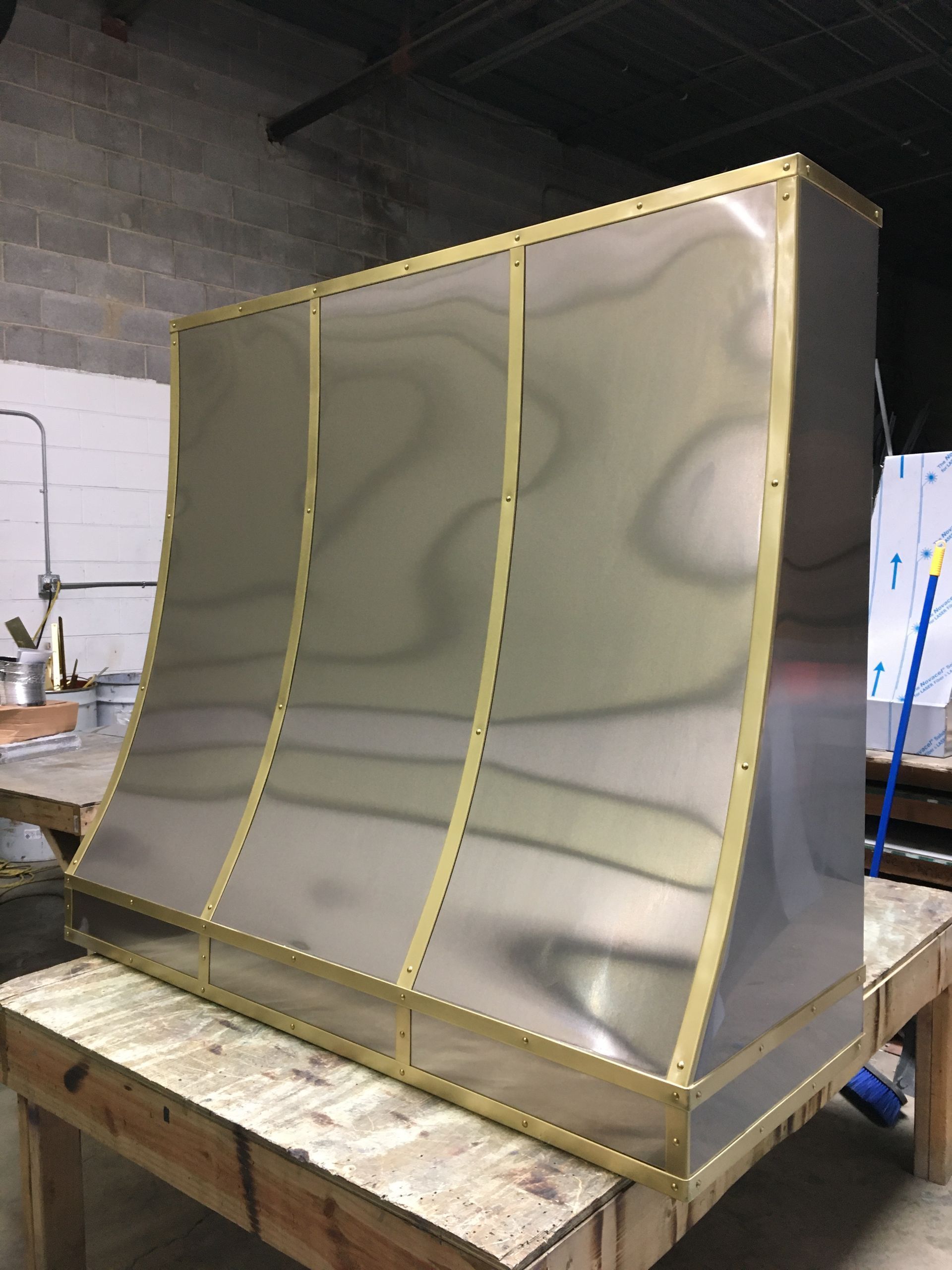 Large stainless steel sheet-metal enclosure on a wooden workbench in an industrial workshop