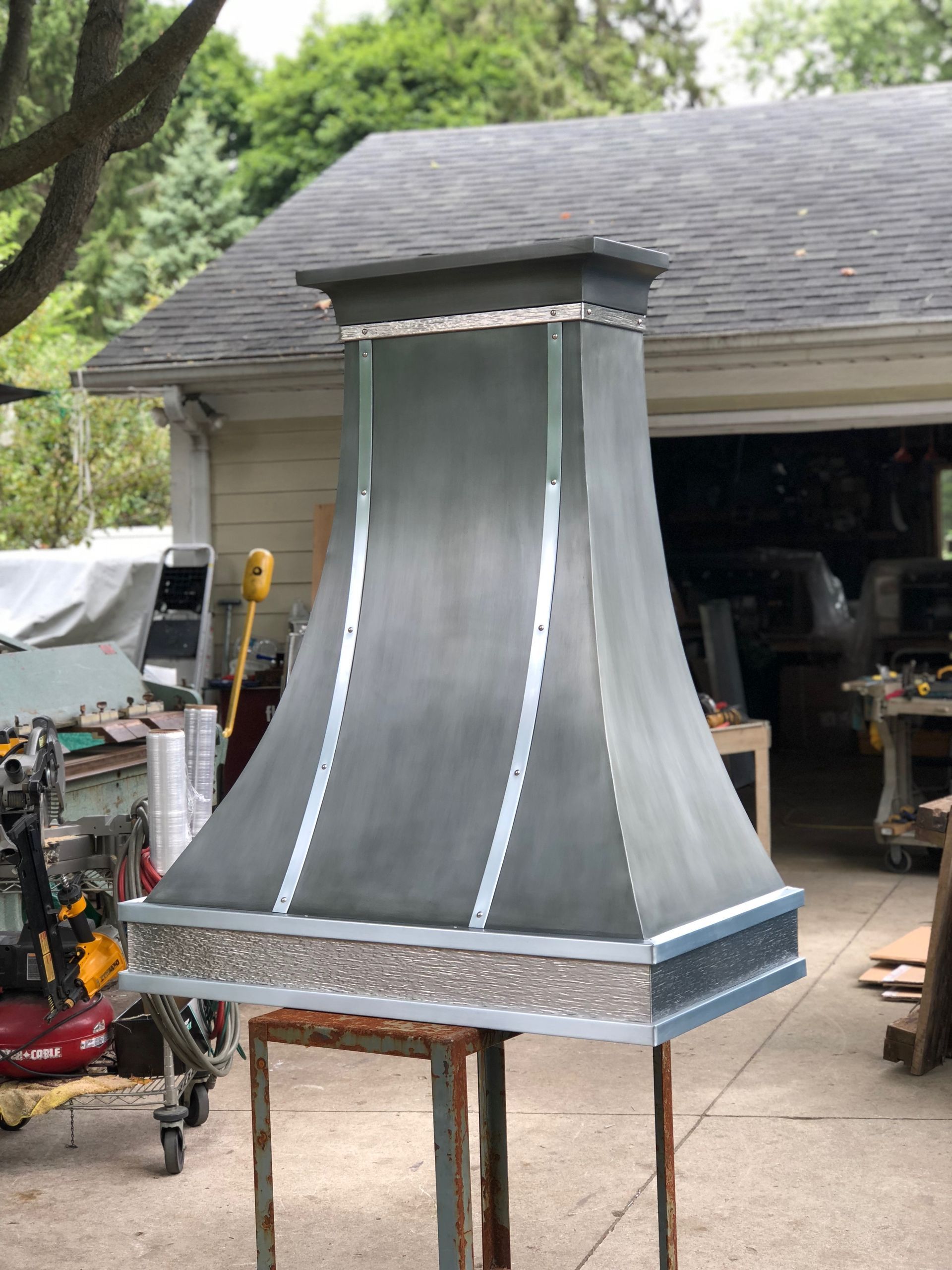 Outdoor metal chimney hood being built on a workbench in a garage.