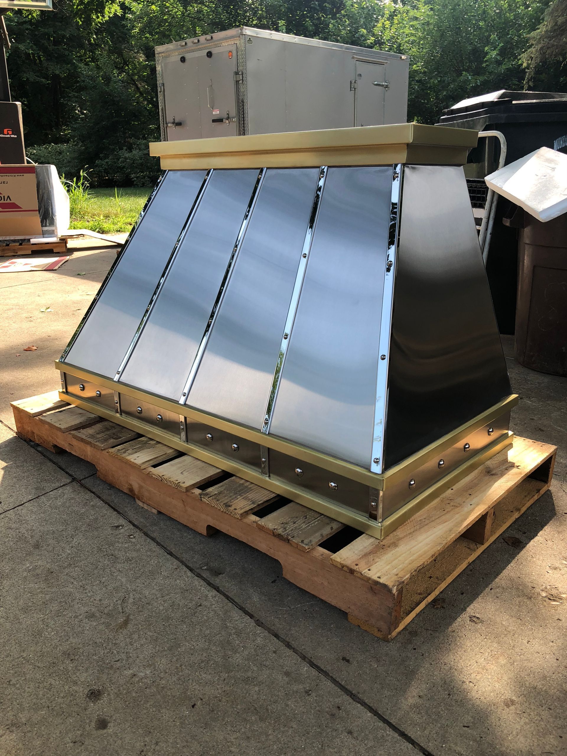 Metal HVAC unit on a wooden pallet outdoors in sunlight, with a cardboard box on top.