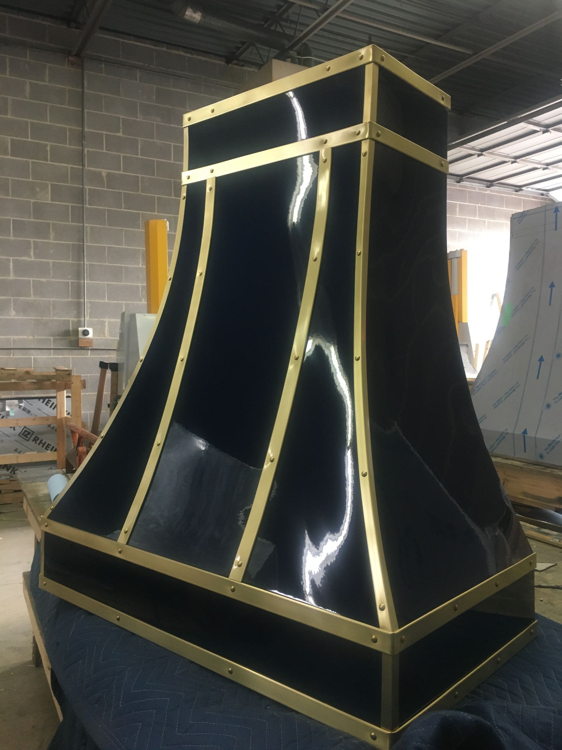 Black-and-gold decorative stage prop or column in a workshop, with reflective curved panels and gold trim