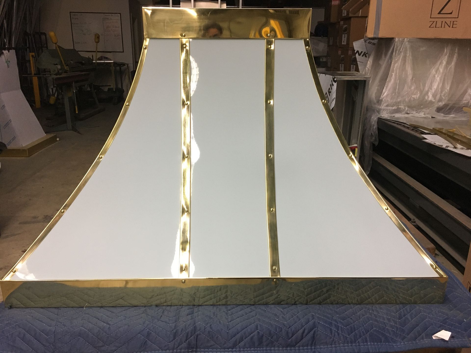 Large white reflective metal sheet with gold trim in an industrial workshop