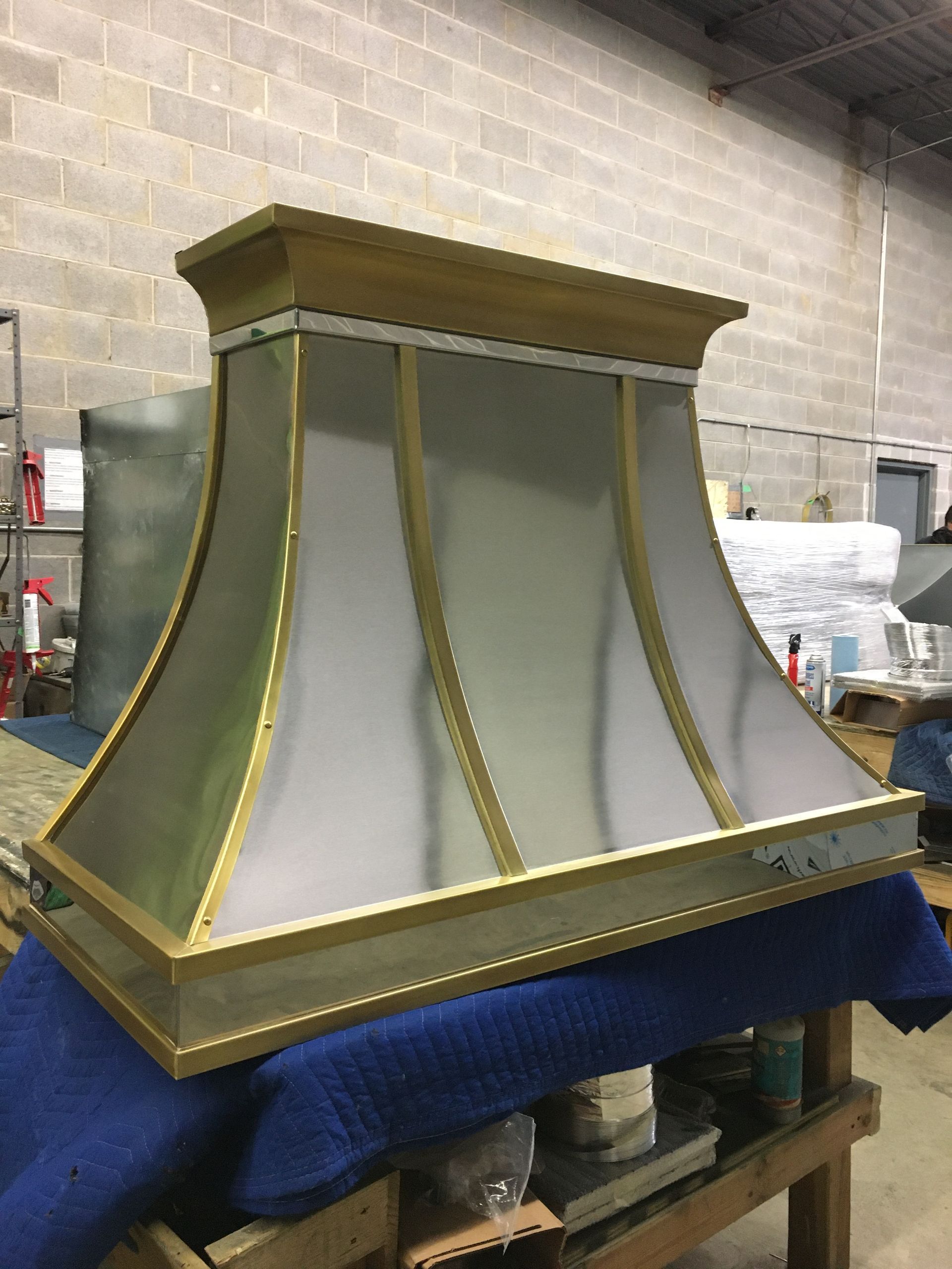 Large gold-trimmed metal hood or lantern-like structure on a blue-covered worktable in a workshop.