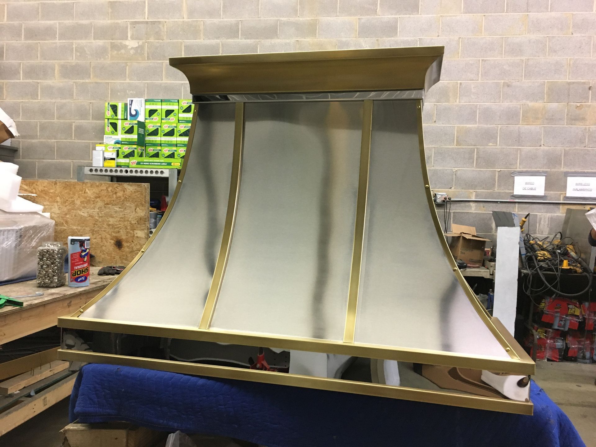 Large metallic funnel-shaped hood with gold trim in a workshop, resting on a blue padded support.