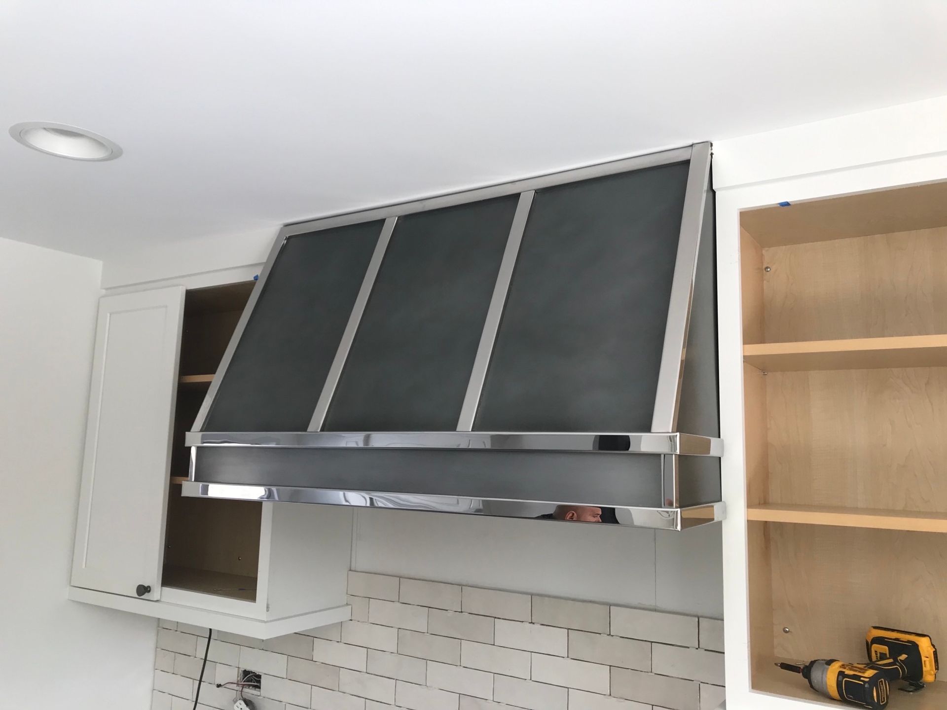 Kitchen with black range hood under white cabinets and exposed wood shelves
