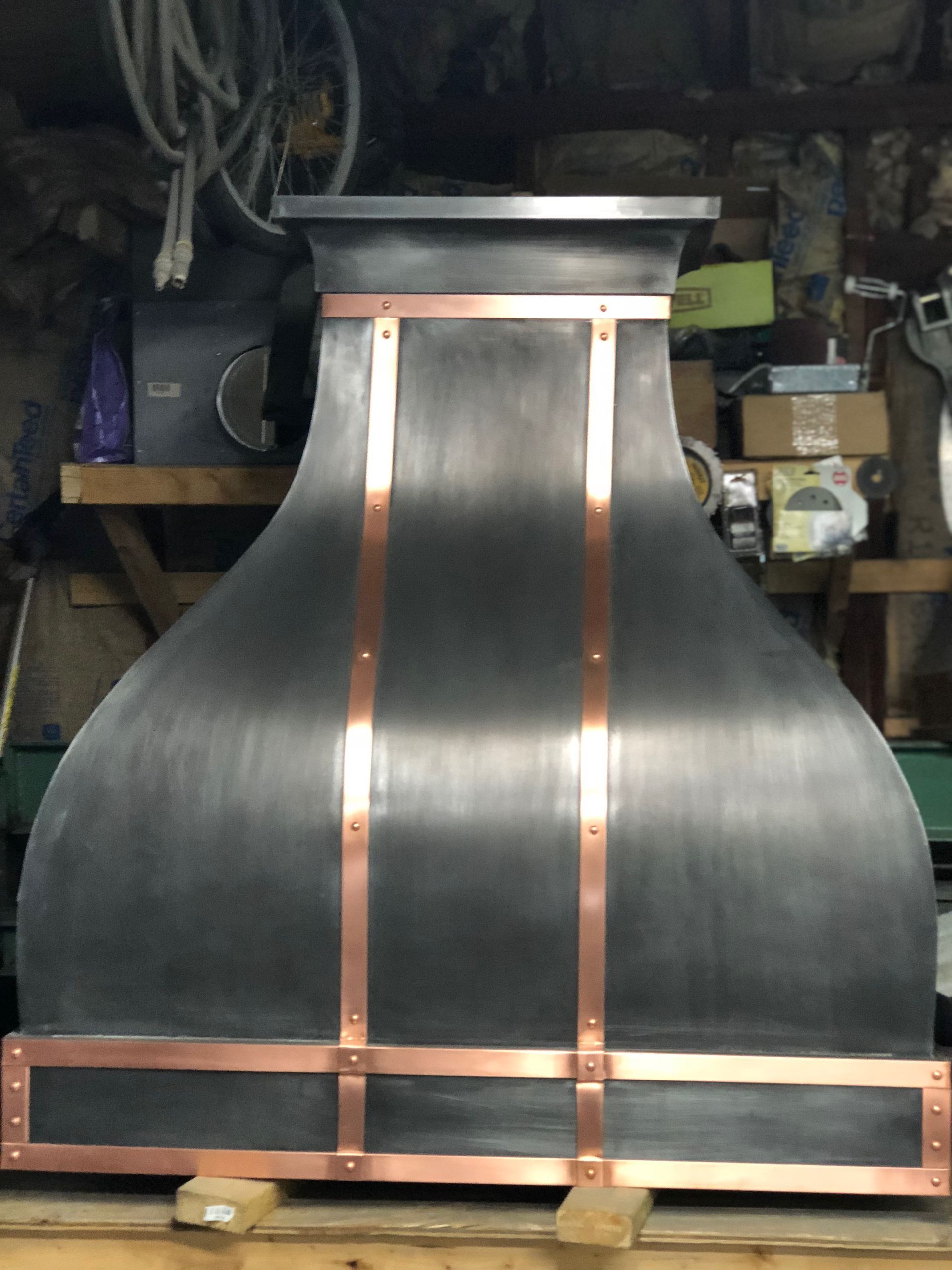 Metal chimney hood with copper trim in a workshop, shown front view