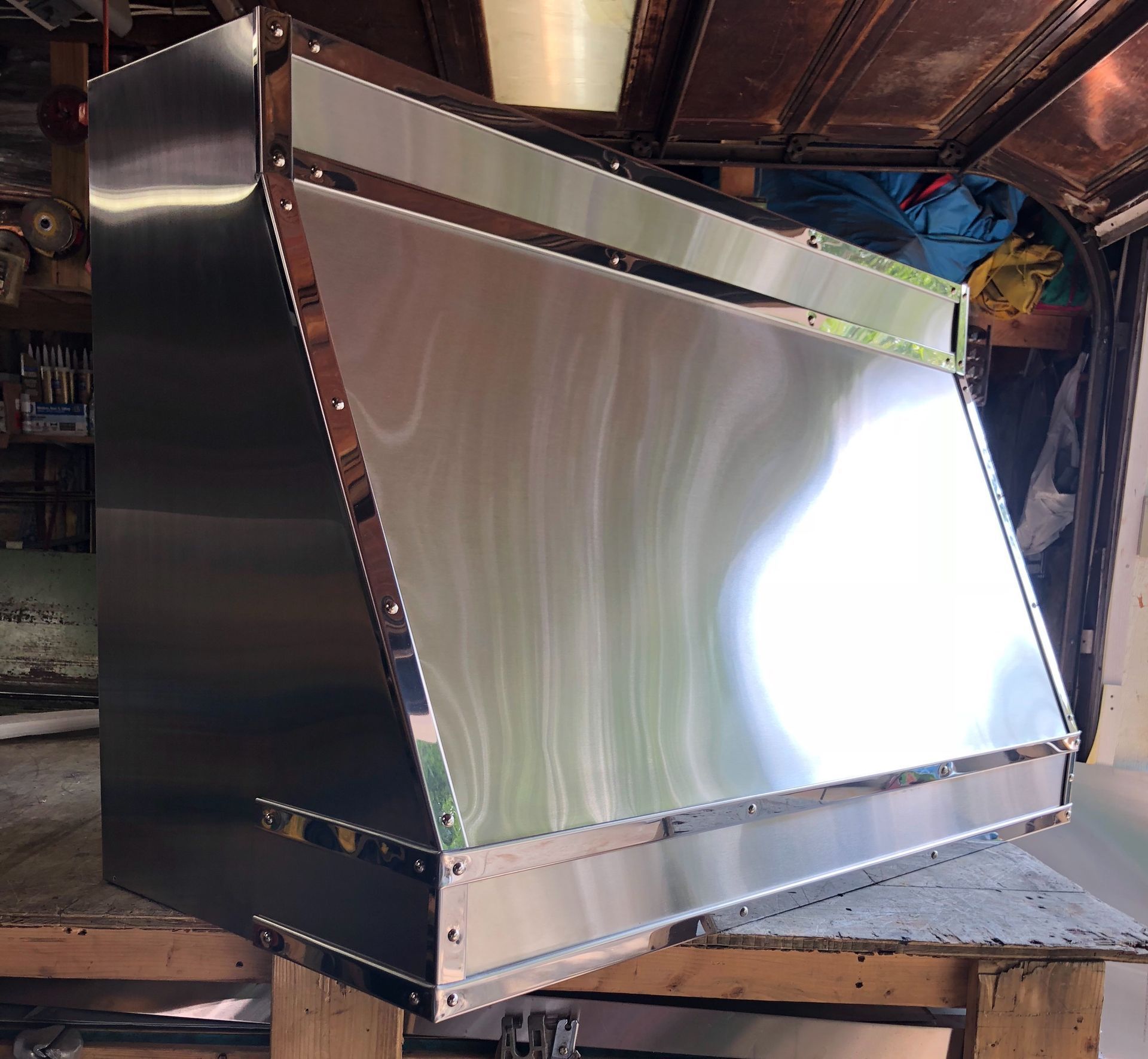Large shiny metal HVAC duct or hood with a reflective front panel in an industrial workshop