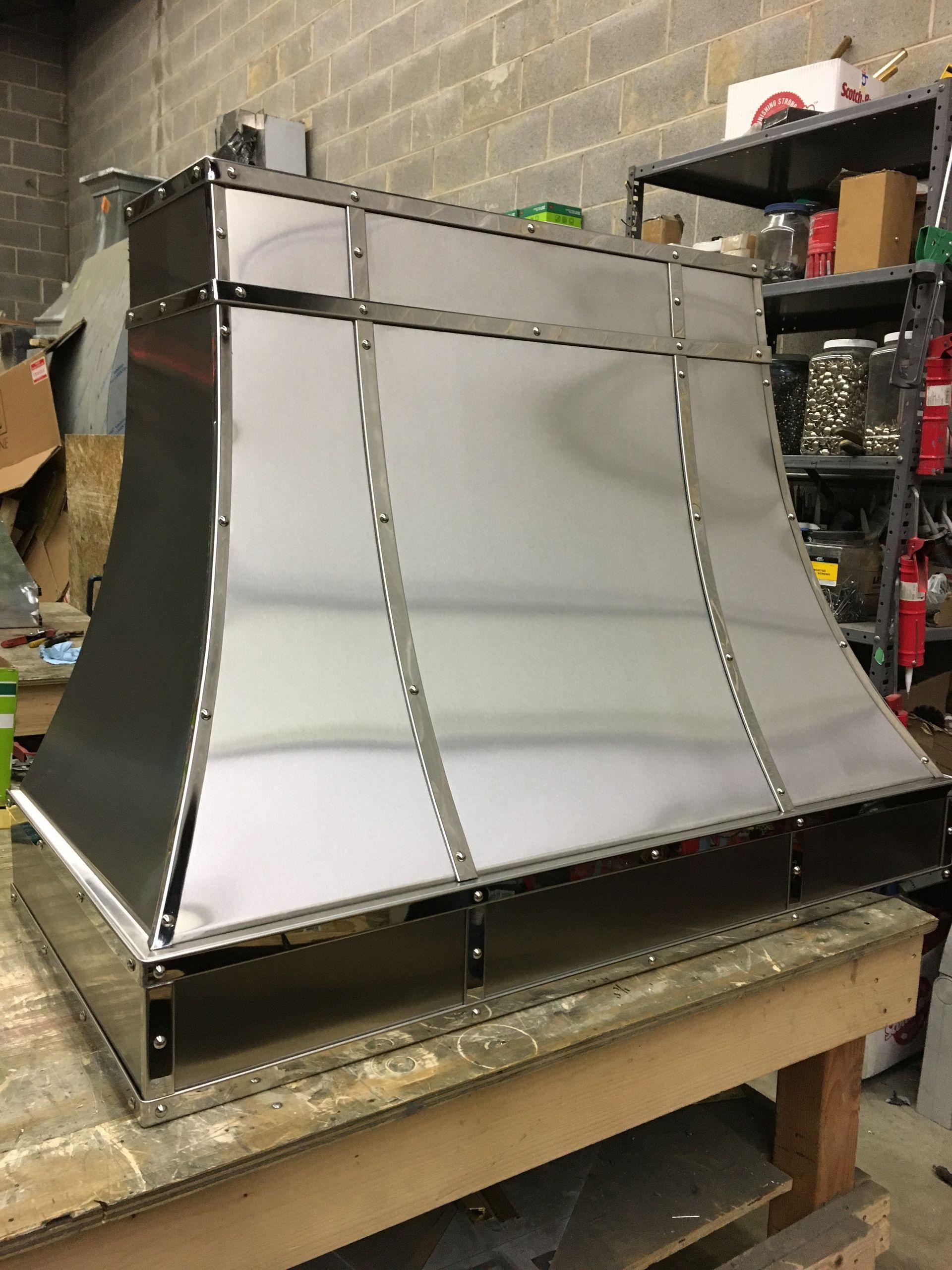 Metal sheet funnel or chute prototype on a workbench in a workshop, with curved silver panels and black framing.