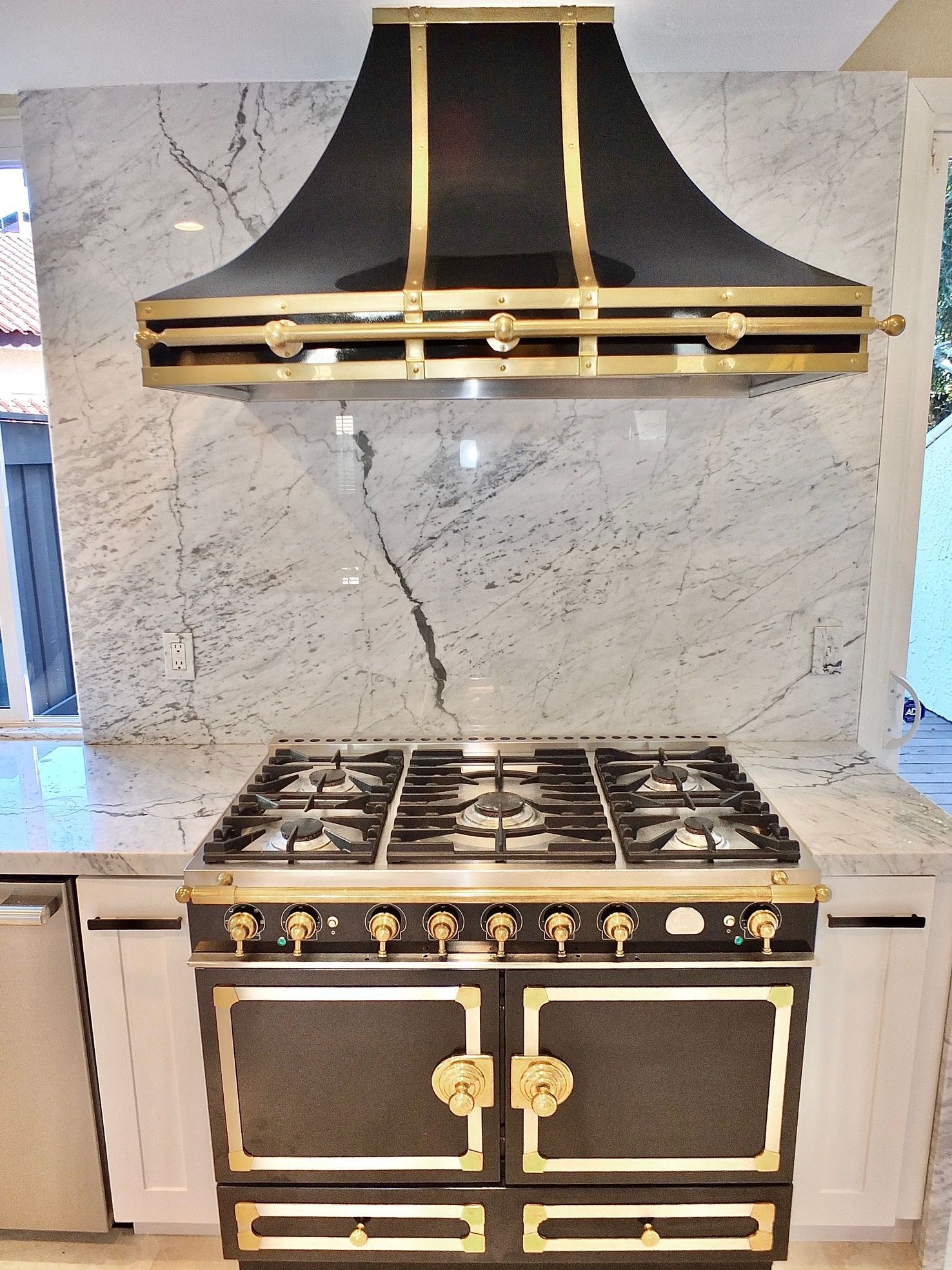 Black-and-gold range with matching hood against a marble backsplash in a modern kitchen