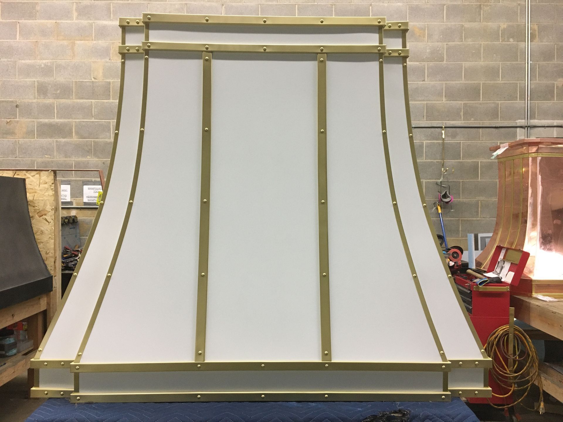 Brass-framed white fireplace surround or decorative panel against a brick wall in a workshop.