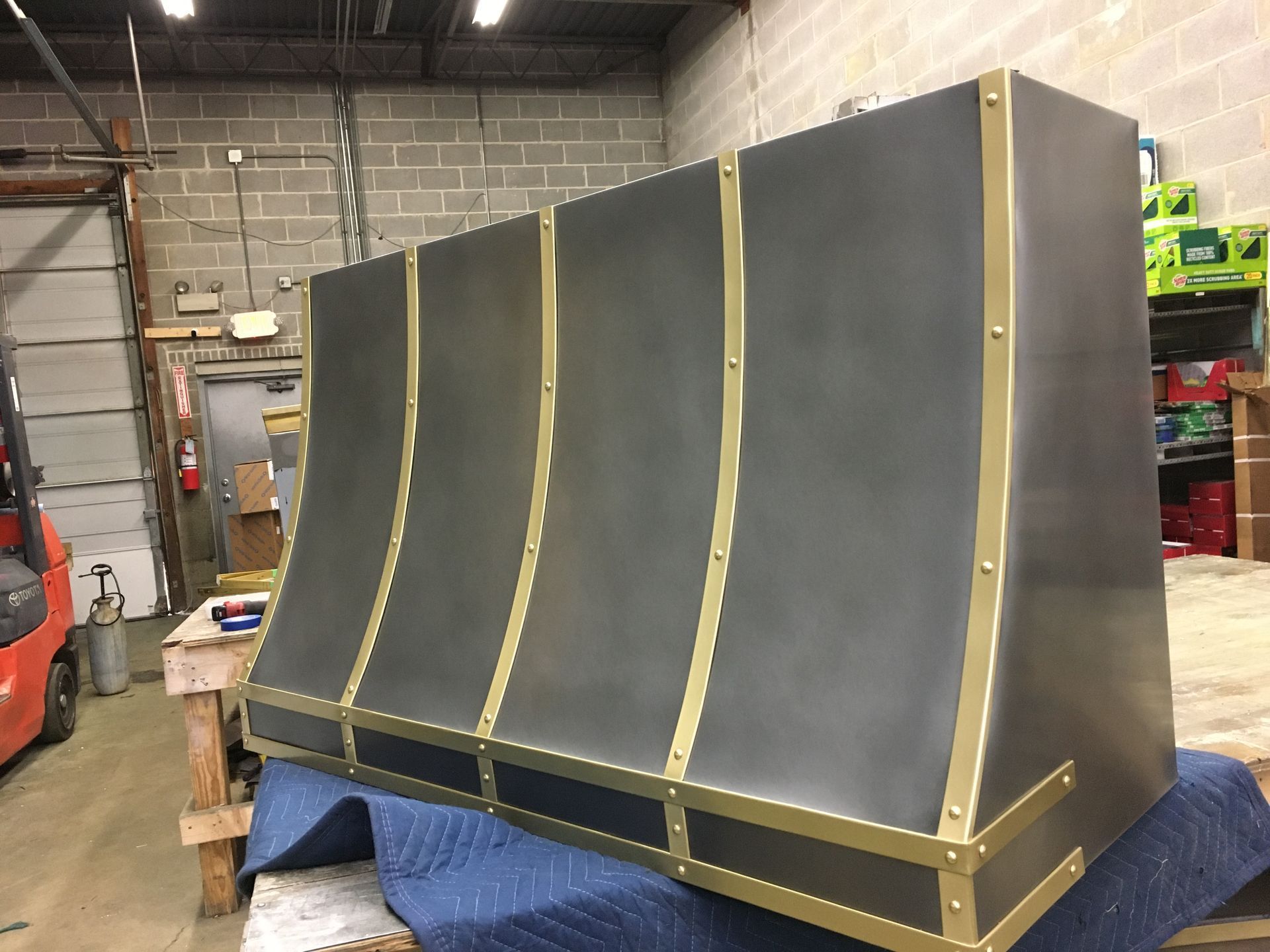Large black-and-gold industrial panel or machine enclosure in a workshop, resting on a blue blanket.