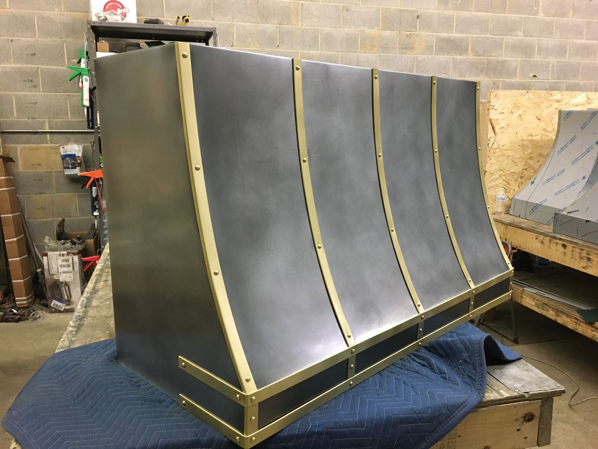 Large black metal industrial part with gold trim, leaning in a workshop against a brick wall.