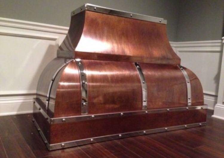 Copper-clad curved wooden chest on a hardwood floor against a paneled wall.