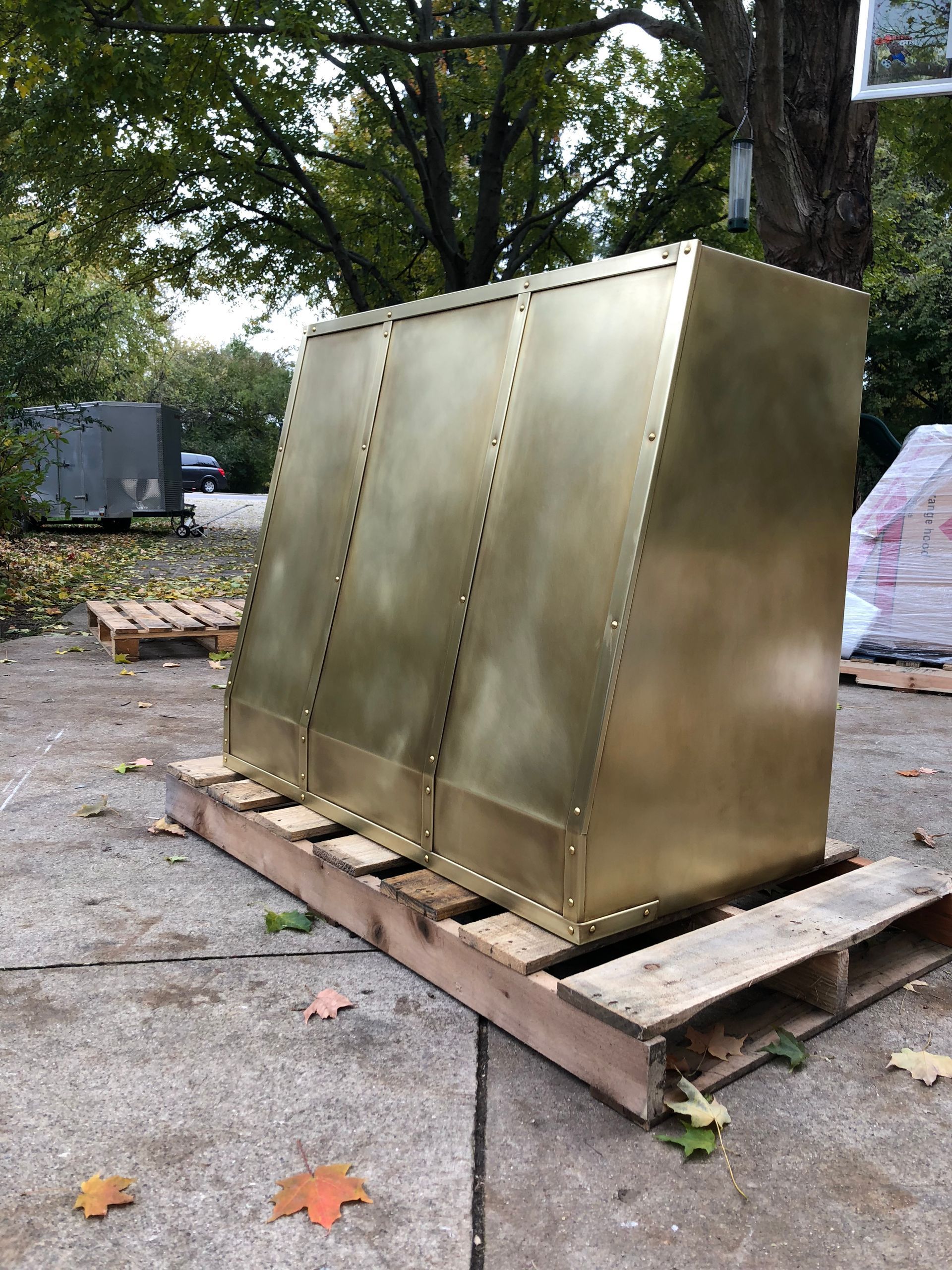 Large gold metal box or cabinet sitting on wooden pallets outdoors under trees