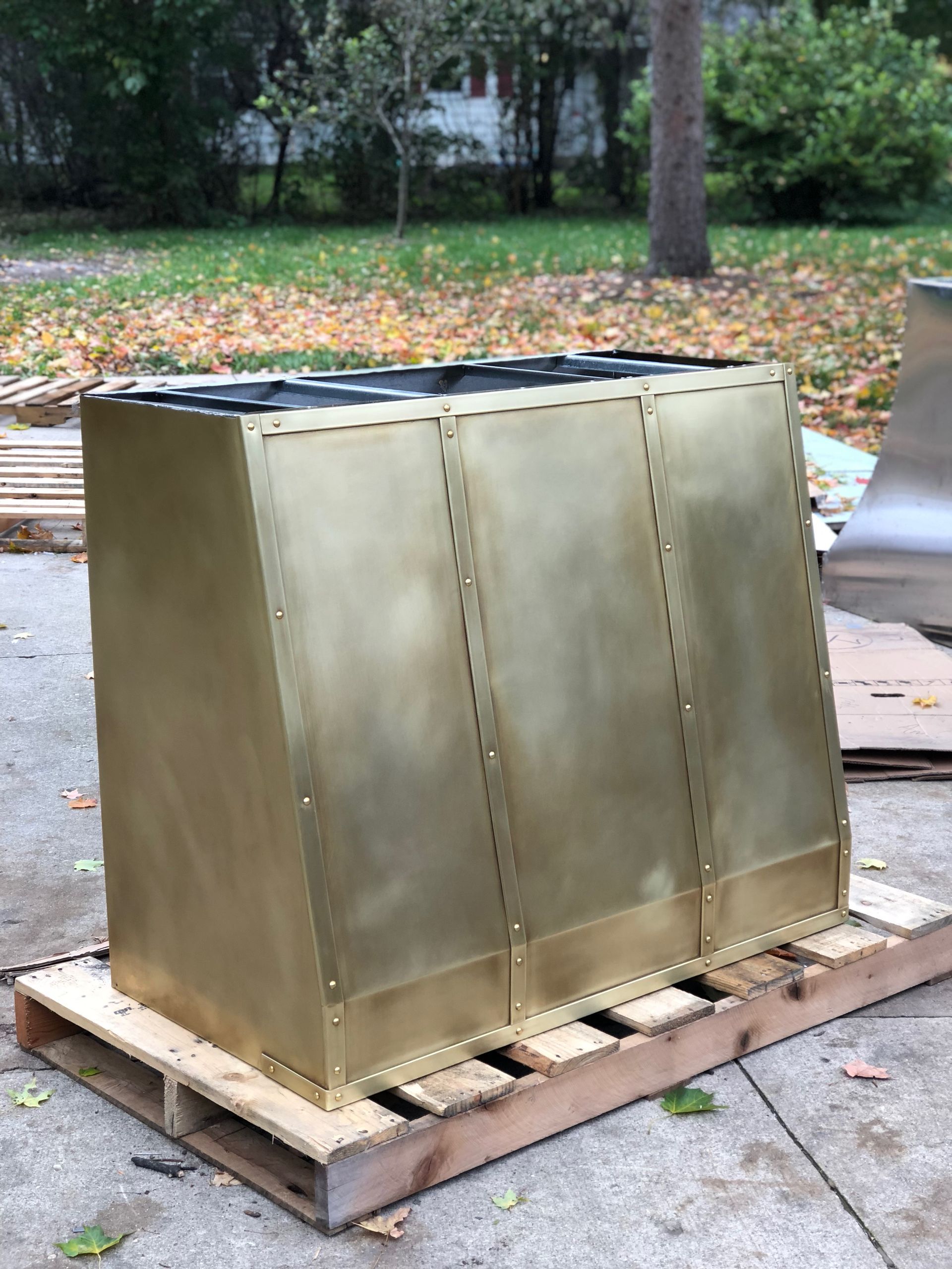 Metal box-like container on a wooden pallet outdoors, with a grassy yard and trees in the background
