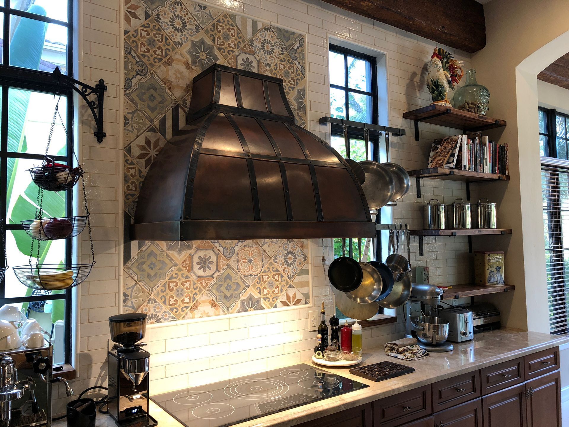 Rustic kitchen with copper range hood, patterned tile backsplash, and counter appliances by bright windows