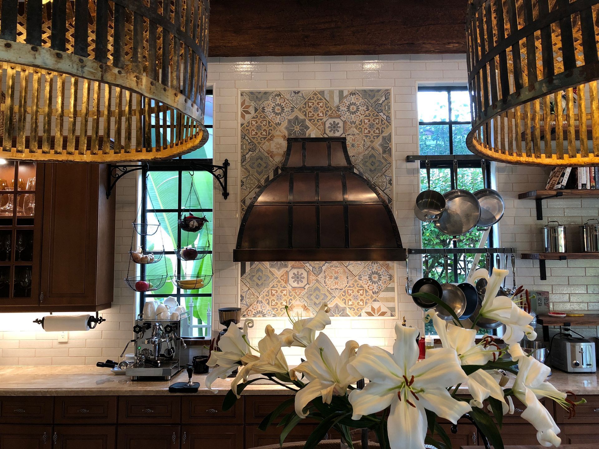 Stylish kitchen with copper hood, patterned backsplash, pendant lights, and white lilies on the counter