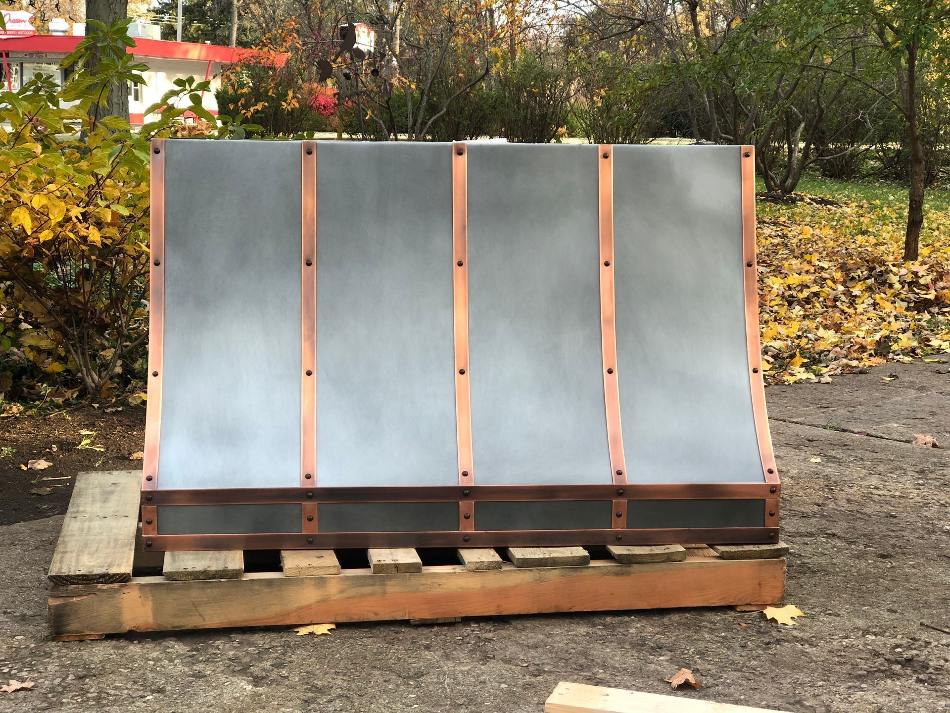 Three-panel solar dryer with silver reflective panels on a wooden base outdoors in a yard.