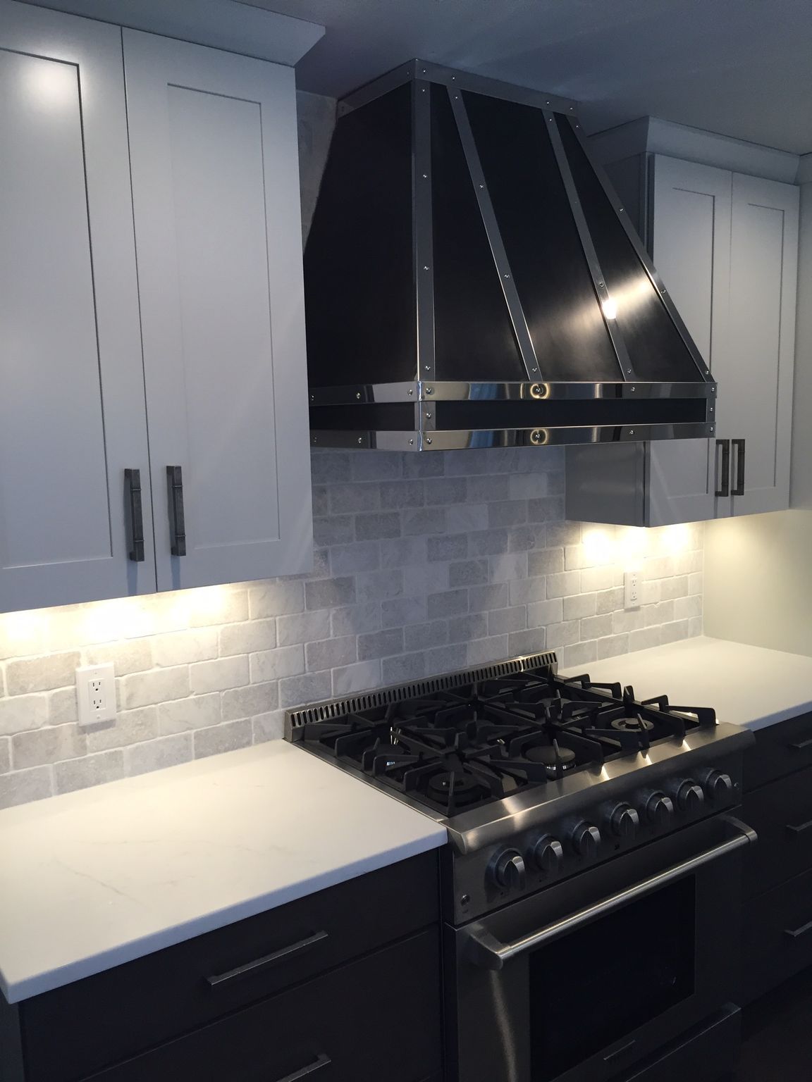 Modern kitchen with white cabinets, black range hood, gas stove, and light gray backsplash