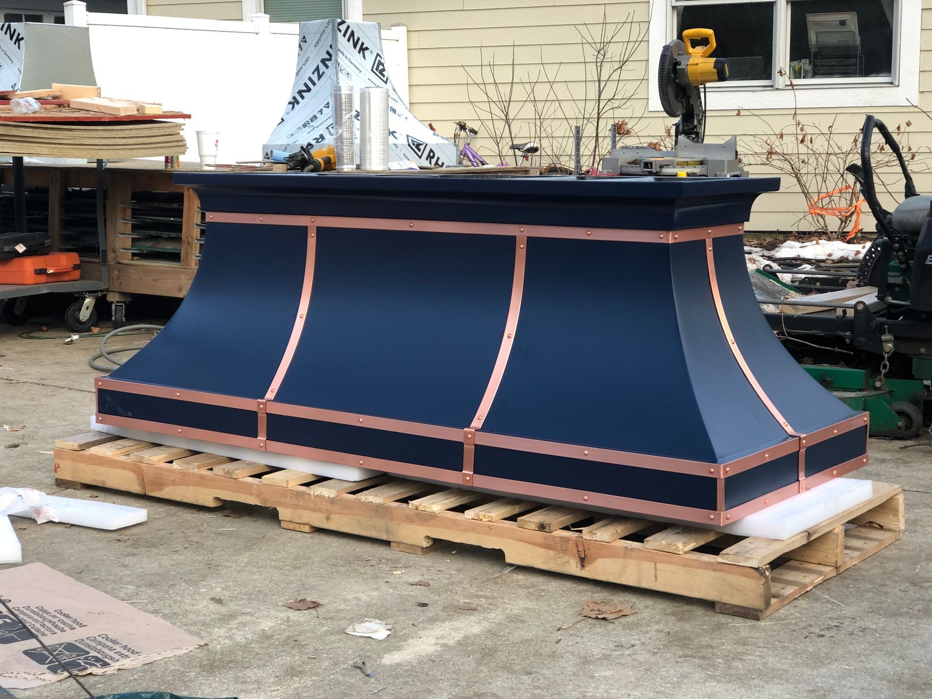 Dark blue decorative pedestal with copper trim on a wooden pallet outdoors