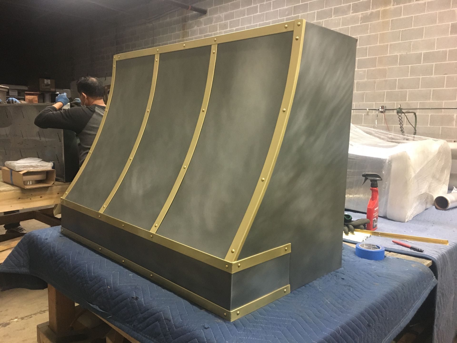 Large black-and-gold curved metal panel on a workbench in a workshop.