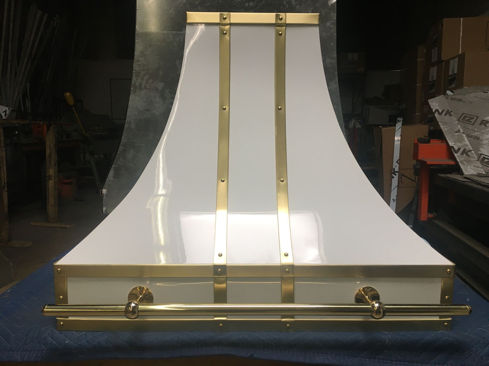 White and gold metal display fixture with curved sides, shown in a workshop or warehouse.