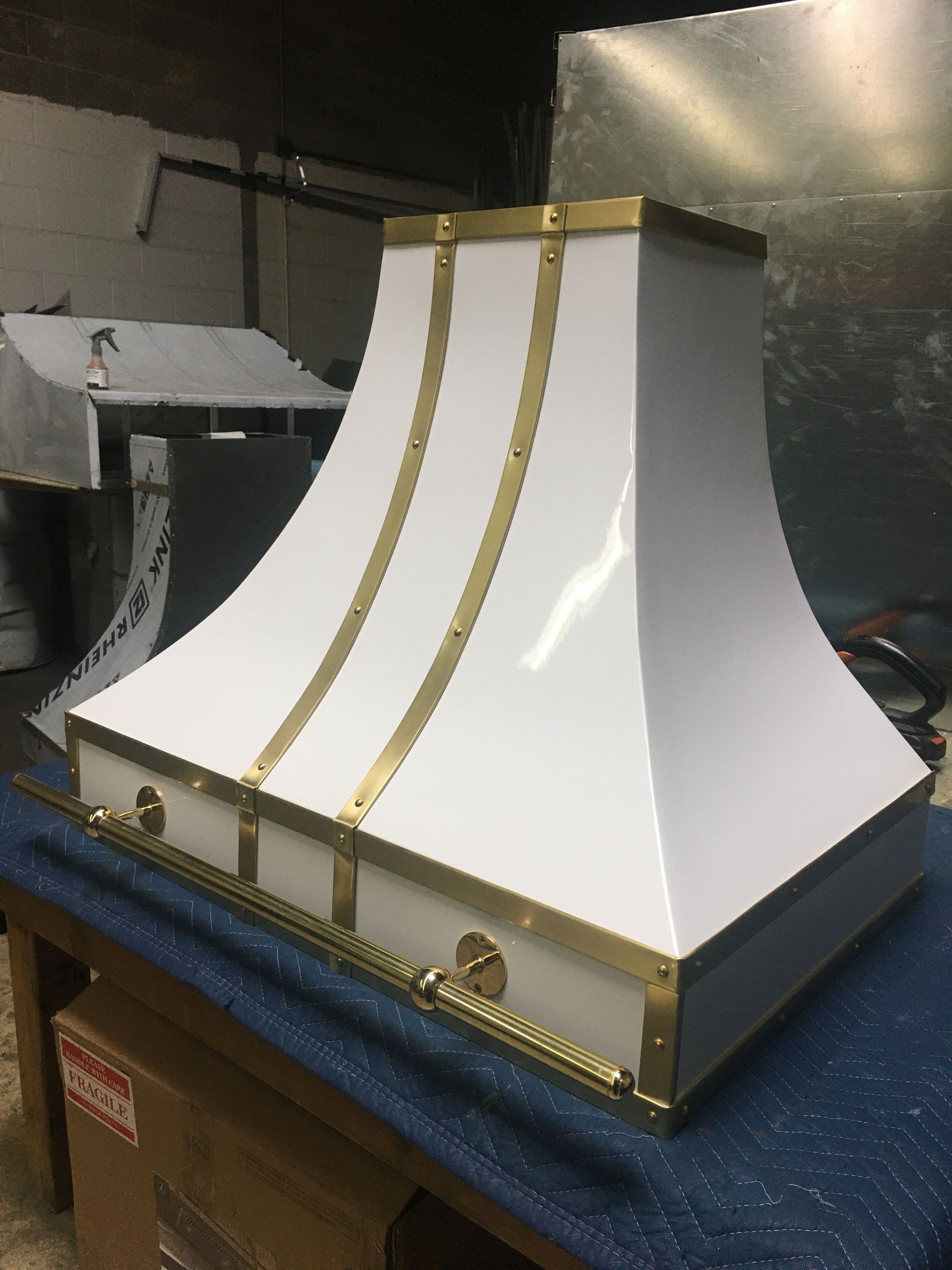 White, gold-trimmed decorative hood or cover on a blue worktable in a workshop