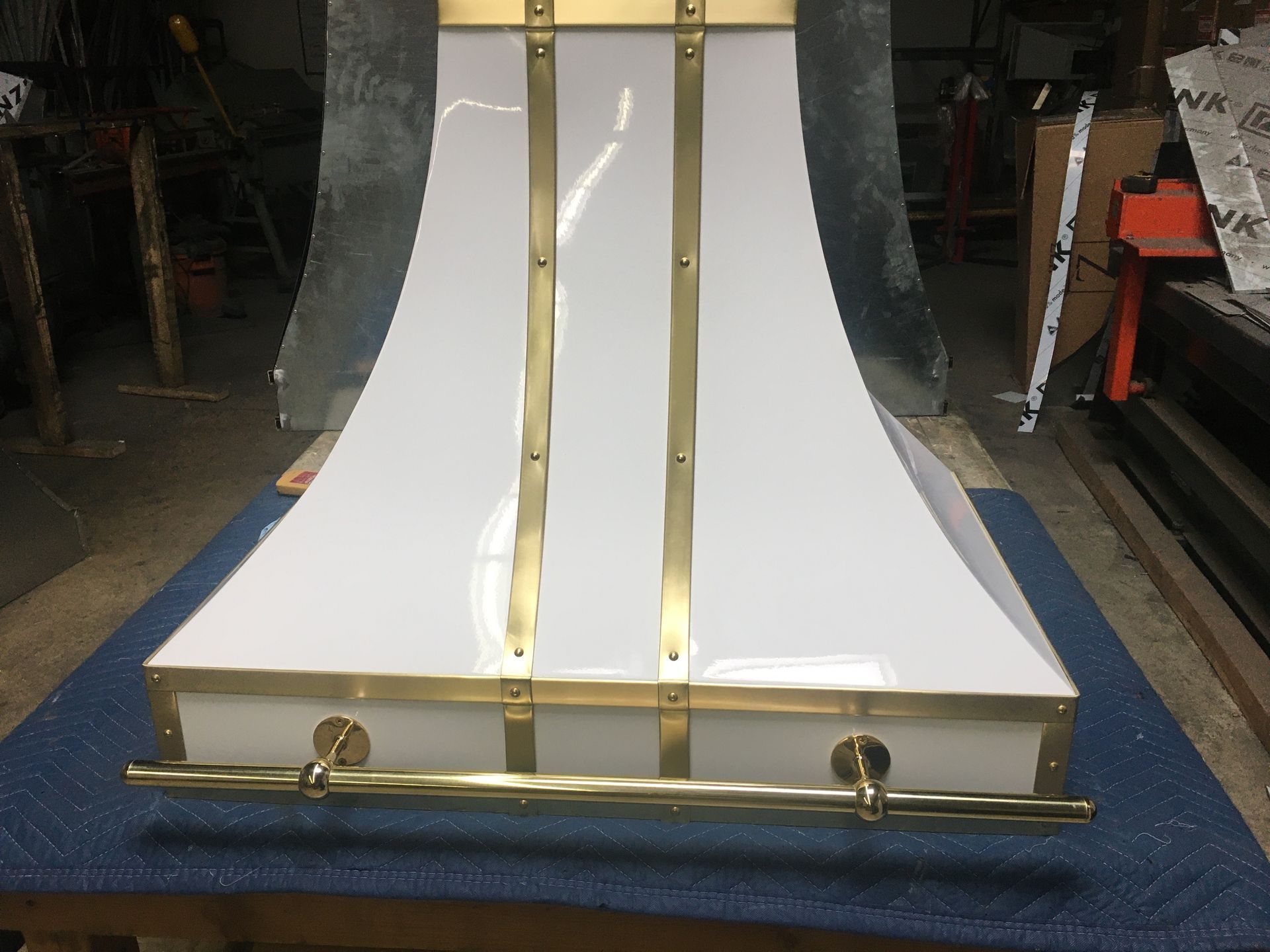 White curved panel with gold trim and hardware, displayed on a blue padded surface in a workshop