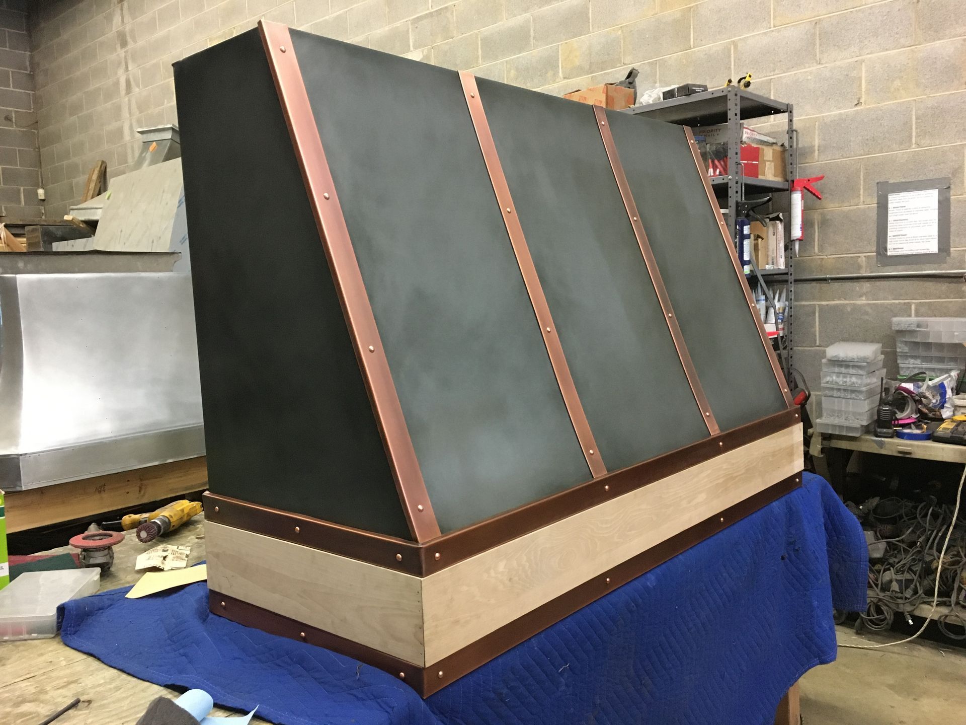 Large black-and-copper hood or enclosure on a workbench in a workshop, with cinder block walls behind it