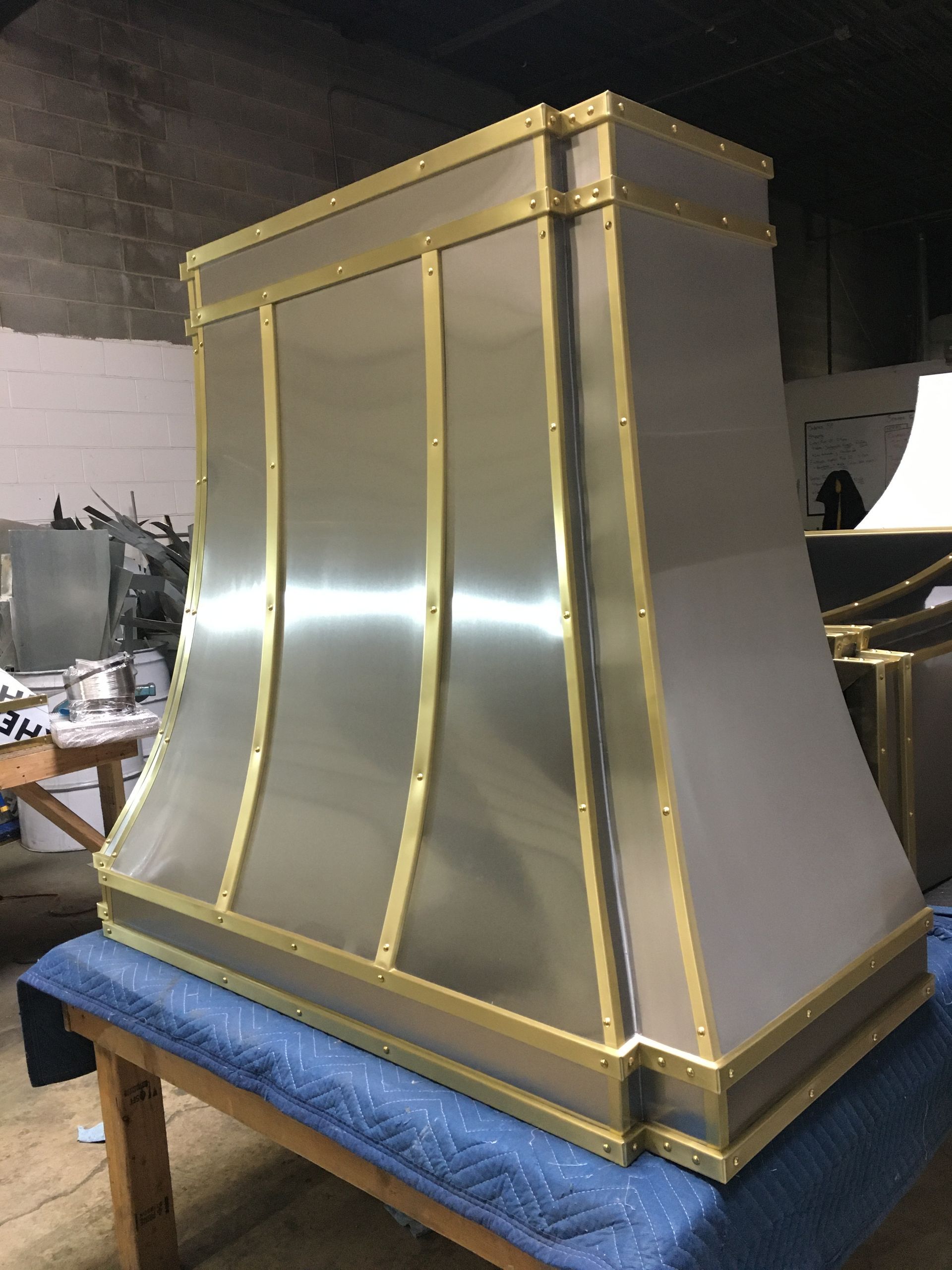 Large silver metal hood with gold trim on a blue padded platform in a workshop