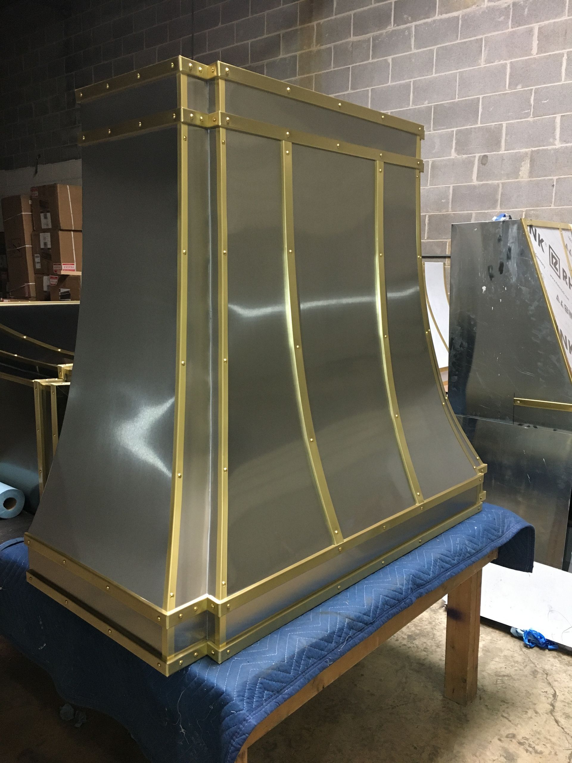 Gold-trimmed metallic fireplace hood on a blue bench in a workshop or showroom