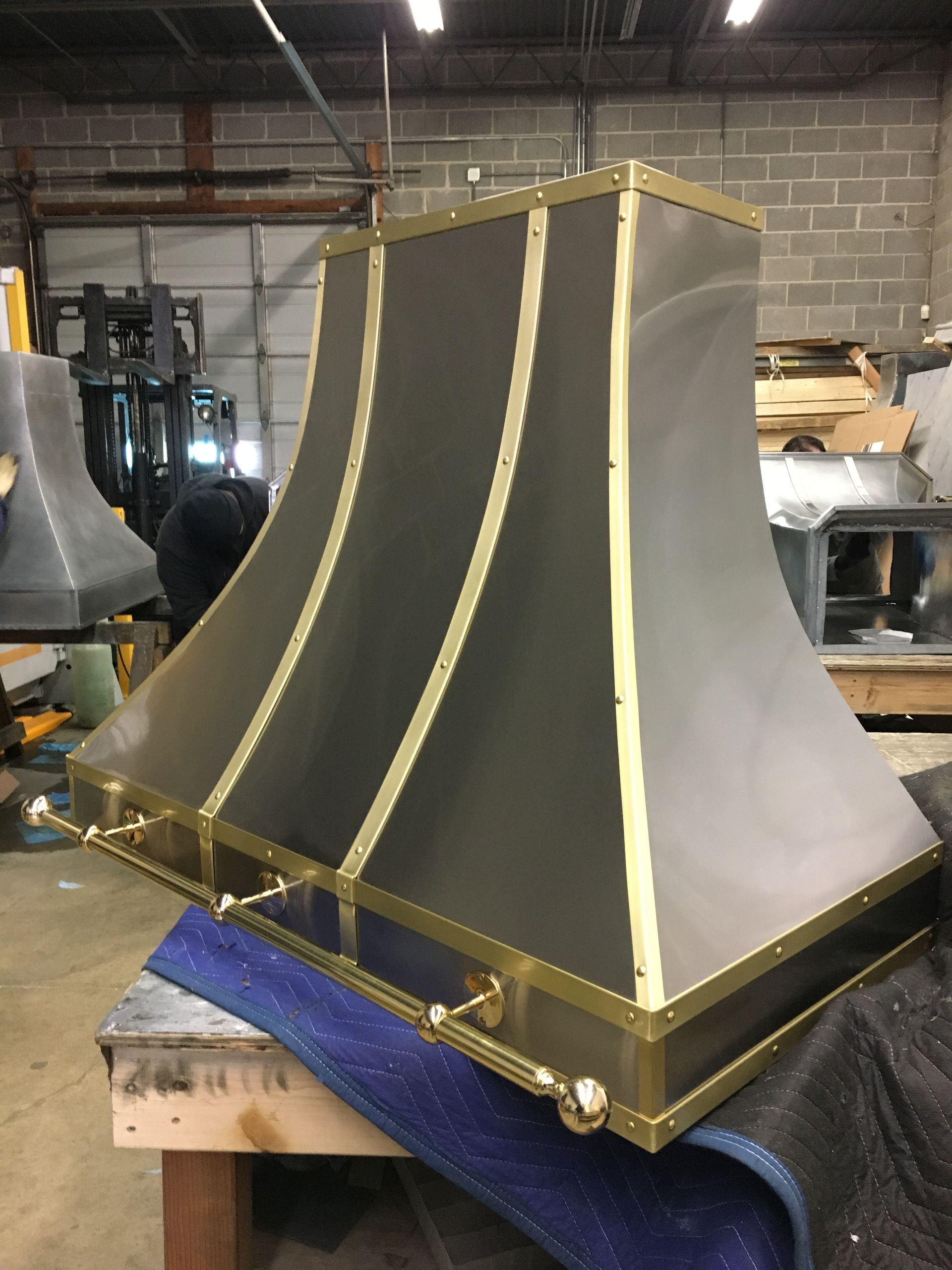 Black metal chimney hood with gold trim, sitting on a workshop table