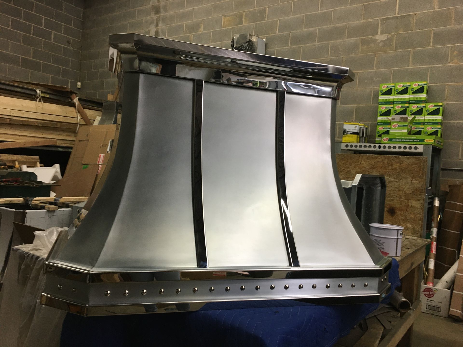 Large metal hood or chimney cover in a workshop, with brushed silver panels and black trim.
