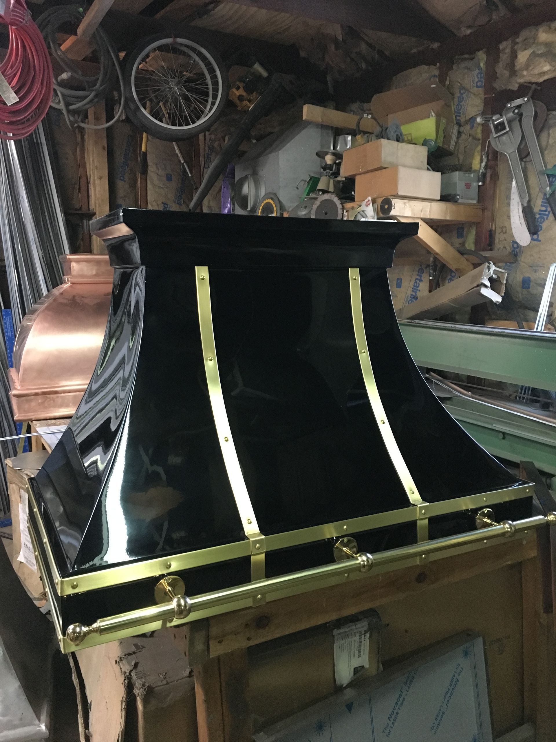 Black curved panel with gold trim in a cluttered workshop, with tools and parts around it
