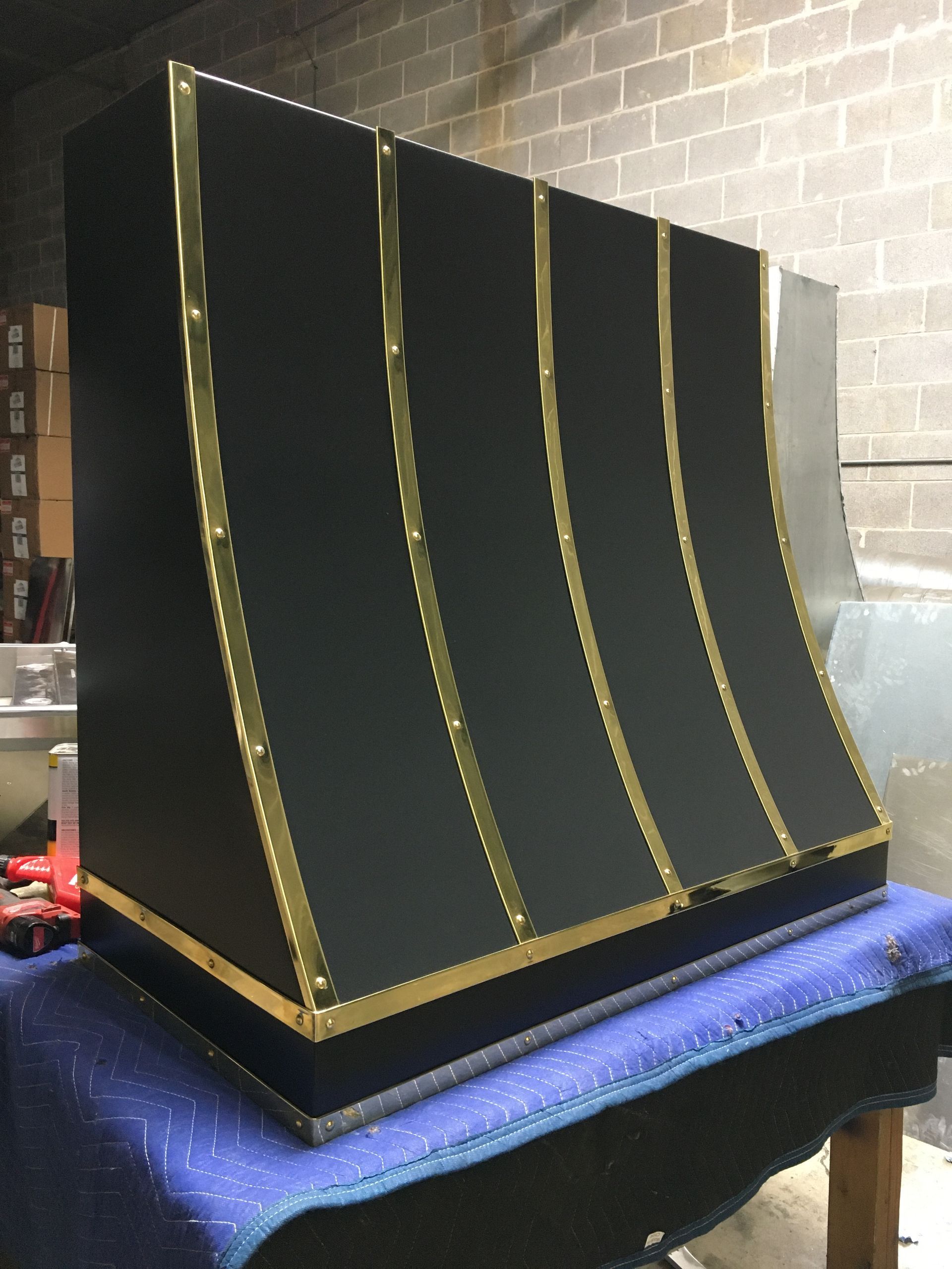Black curved display panel with gold trim on a blue cloth, against a brick wall.